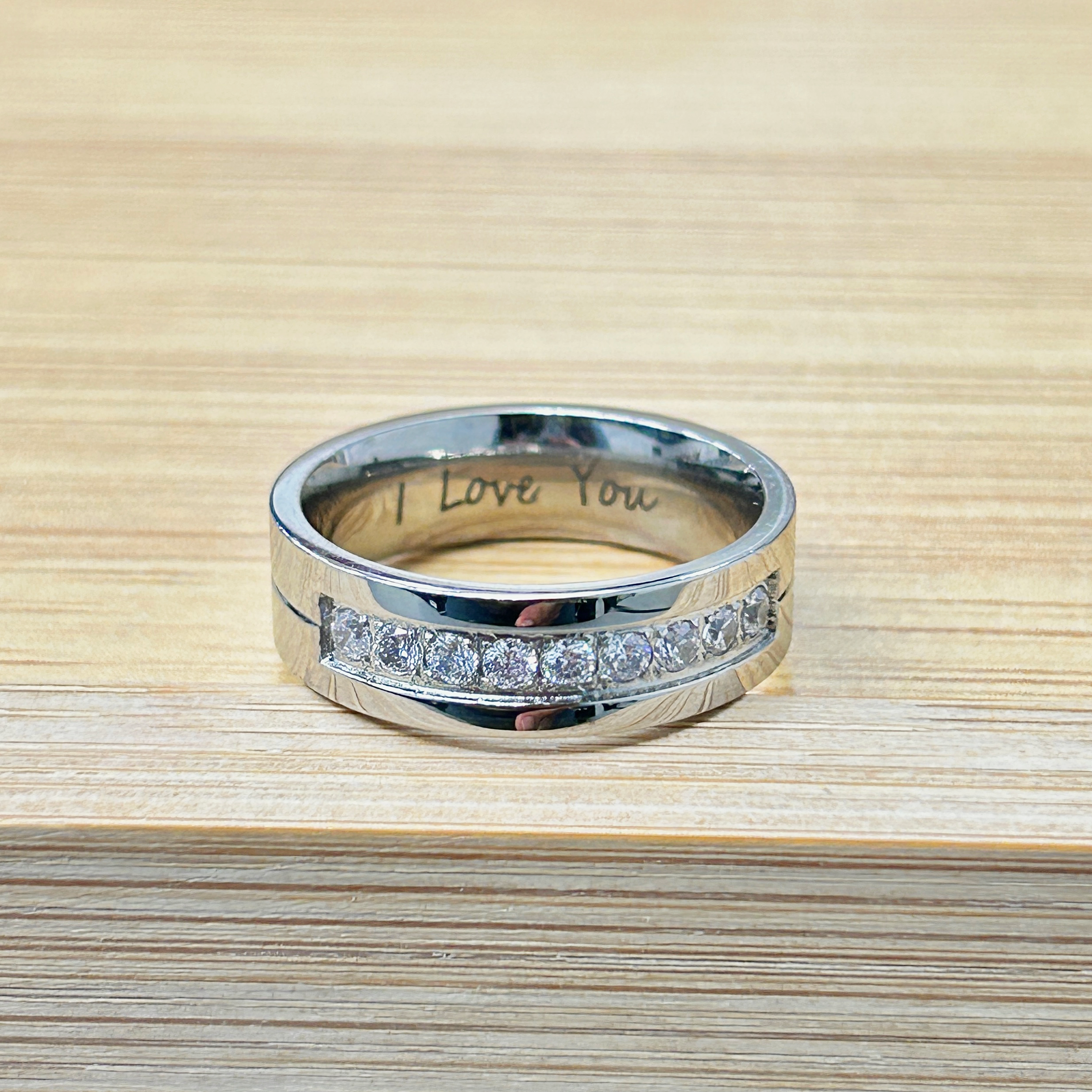 Silver Channel Set I Love You Engraved Ring picture2 - Eriy Gift Silver ring on light wood with the inner engraving 'I love you' visible.