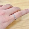 Close-up of a finger wearing a thin silver textured ring on a wooden surface background.