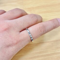 Close-up of a finger wearing a thin silver textured ring on a wooden surface background.