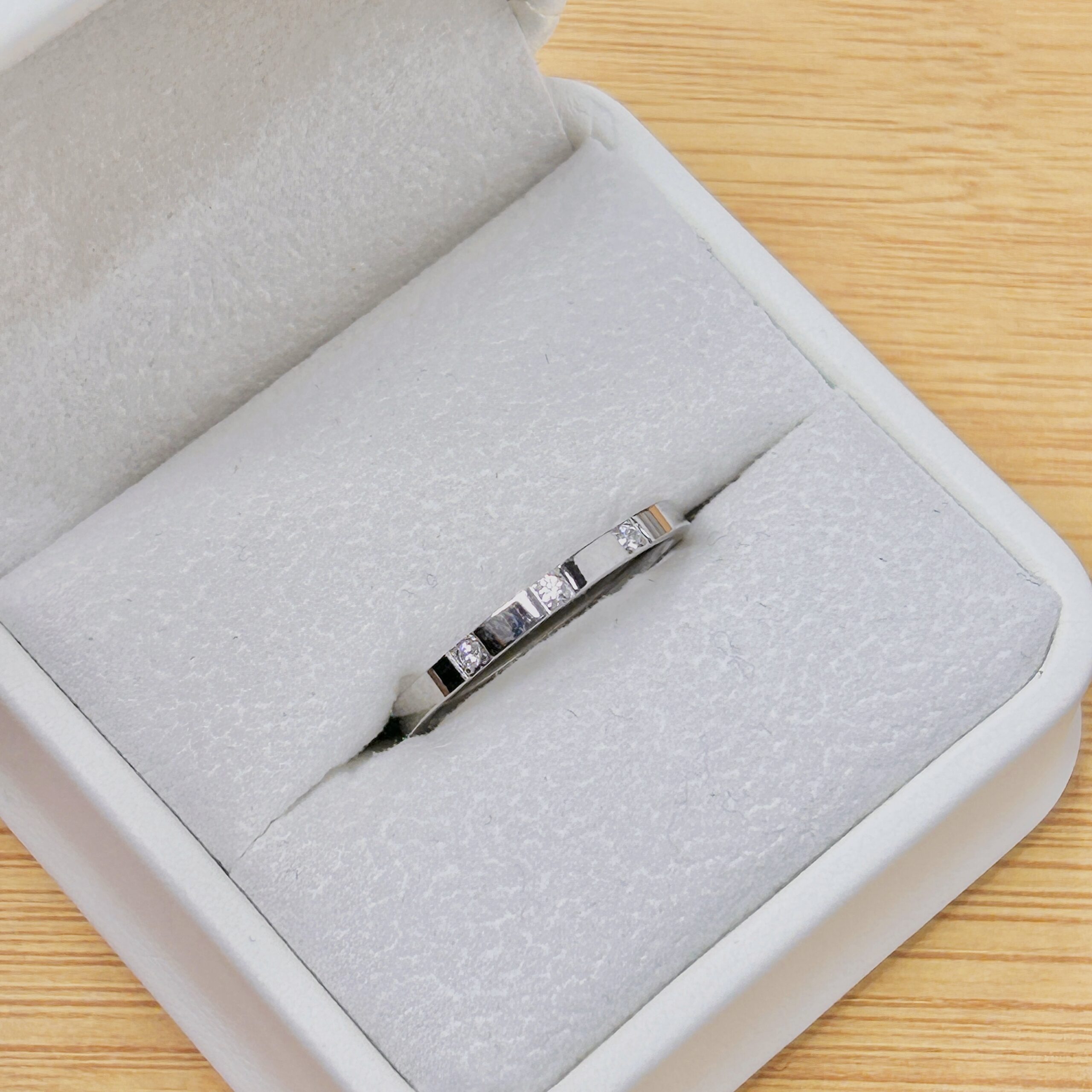 Two silver rings with embedded stones in a gray jewelry box on a wooden surface.