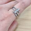 Close-up of a finger wearing two silver rings with diamond stones, on a wooden surface background, highlighting the jewelry.