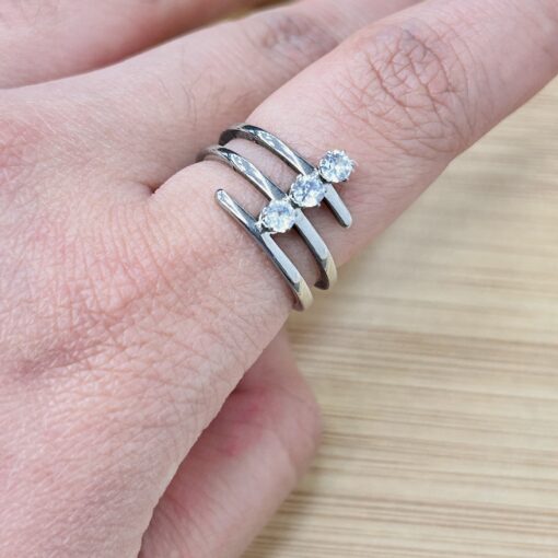 Silver Coil Wrap Three-Stone Zirconia Ring - Eriy Gift Close-up of a finger wearing two silver rings with diamond stones, on a wooden surface background, highlighting the jewelry.