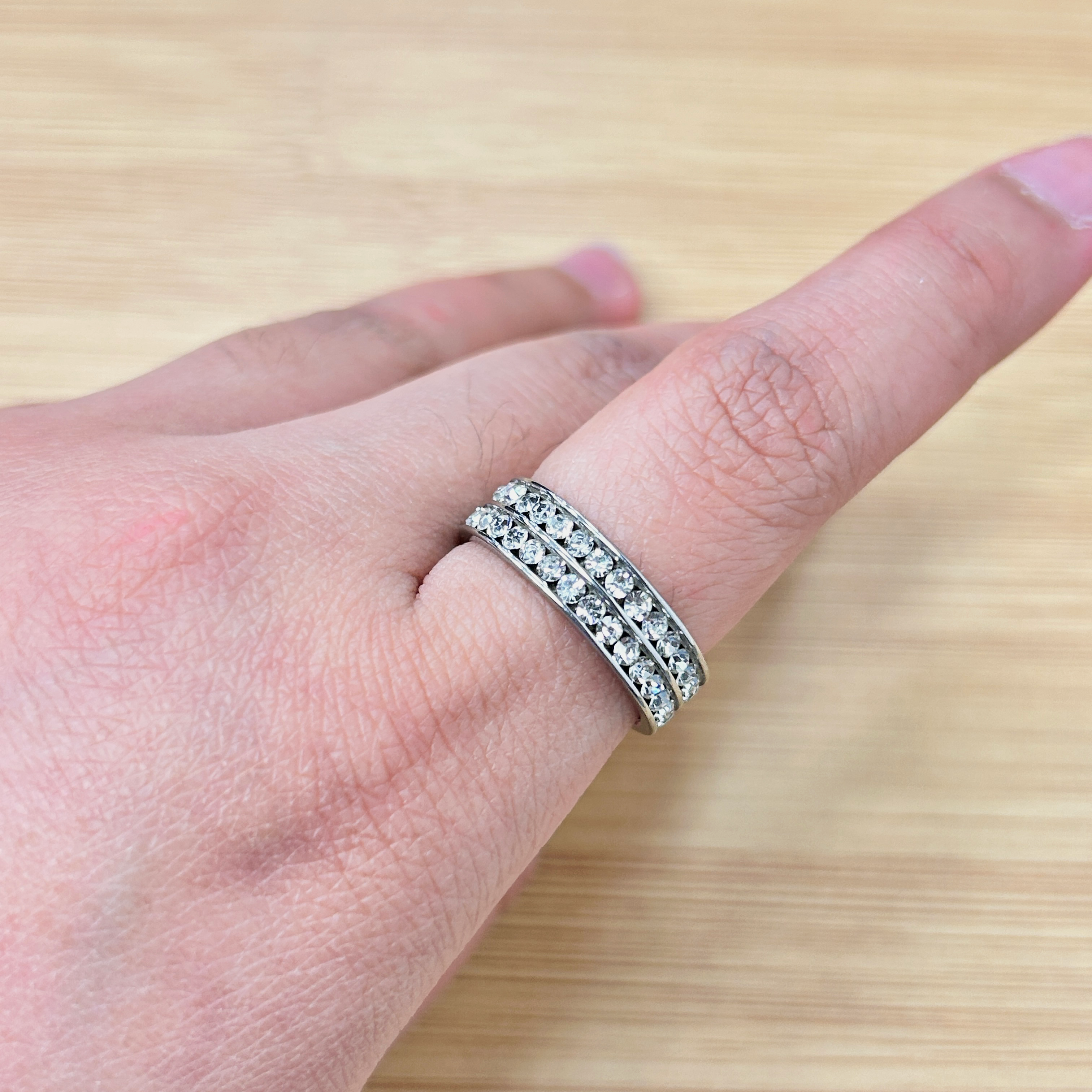 Close-up of a hand wearing two diamond-studded bands on the ring finger, resting on a wooden surface.