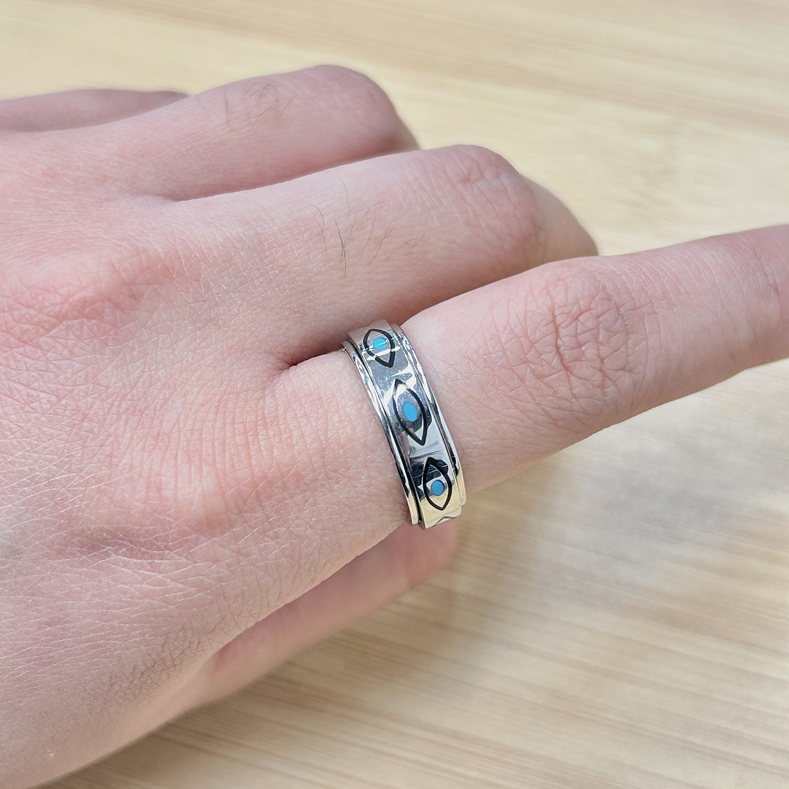 Close-up of a hand wearing a silver ring with blue stones on the ring finger of a light-skinned hand.