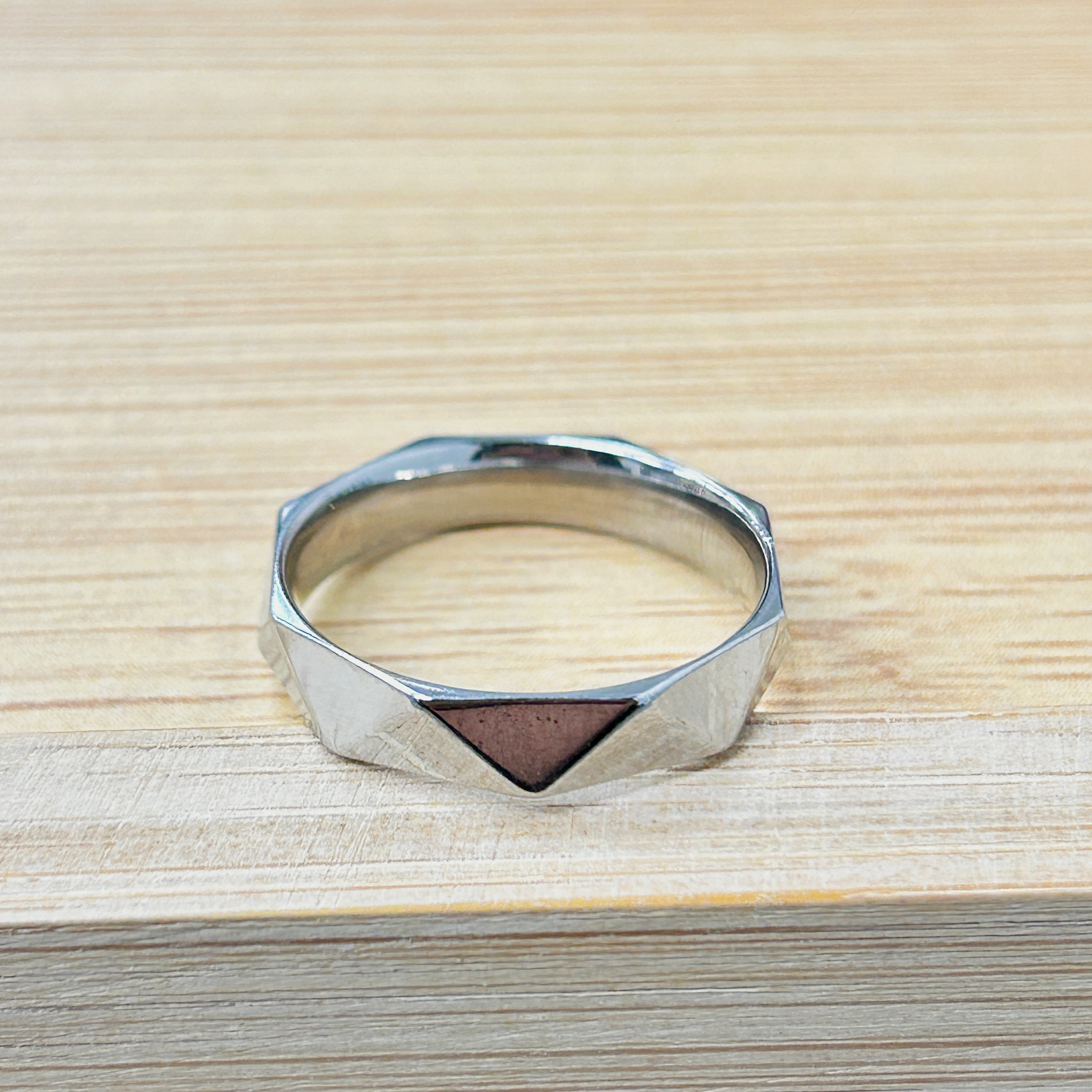 Silver Faceted Triangle Geometric Ring picture2 - Eriy Gift Partial view of a shiny metal ring or bracelet resting on a light wood surface, photographed from above.