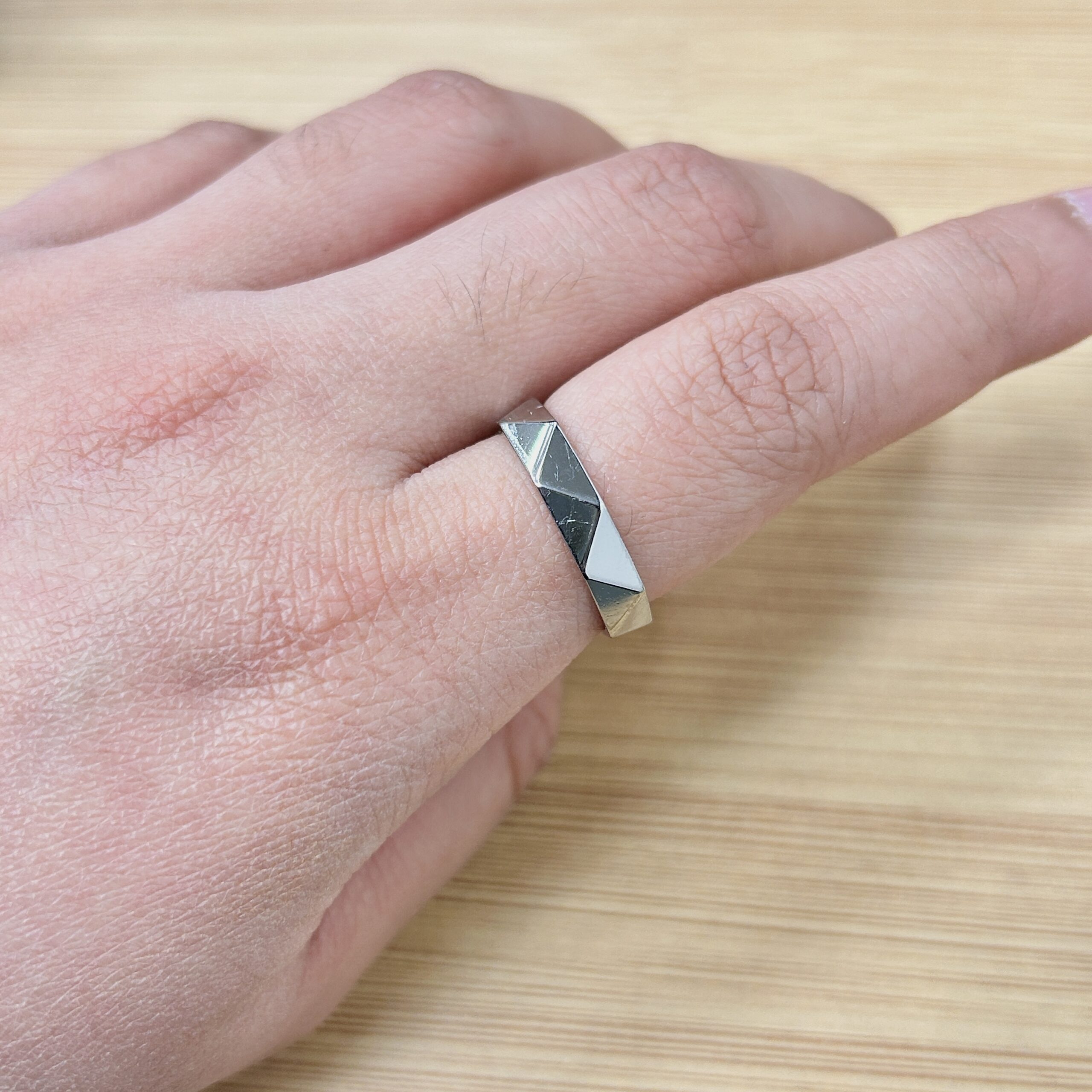 Close-up of a wrist adorned with a silver faceted geometric bracelet on pale skin, resting on a wooden surface.