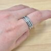 Close-up of a hand with two silver stacked rings on a finger resting on a wooden surface.
