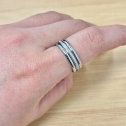 Close-up of a hand with two silver stacked rings on a finger resting on a wooden surface.