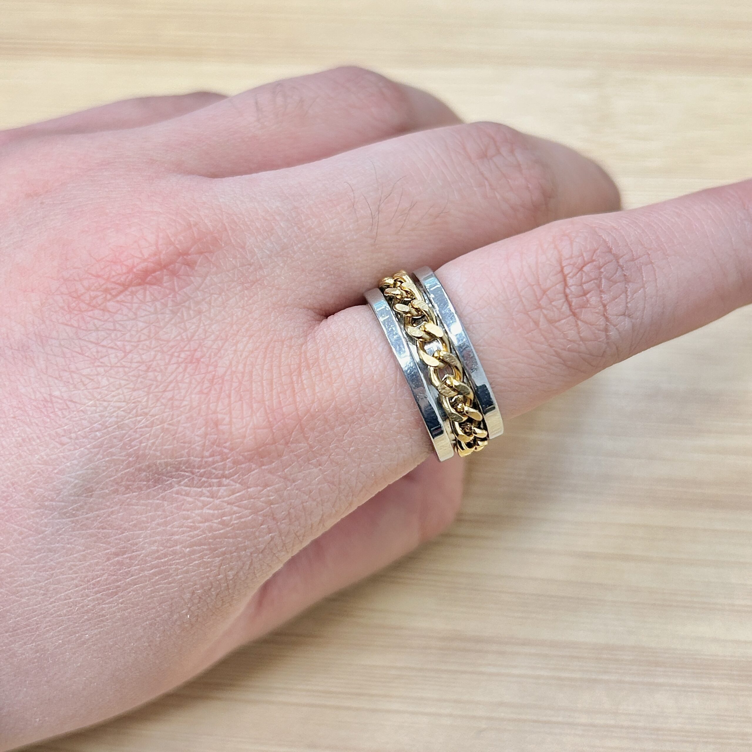 Silver Gold Spinning Cuban Link Chain Ring - Eriy Gift Close-up of a wrist wearing a two-tone ring with a gold chain detail on a light wooden surface behind it.
