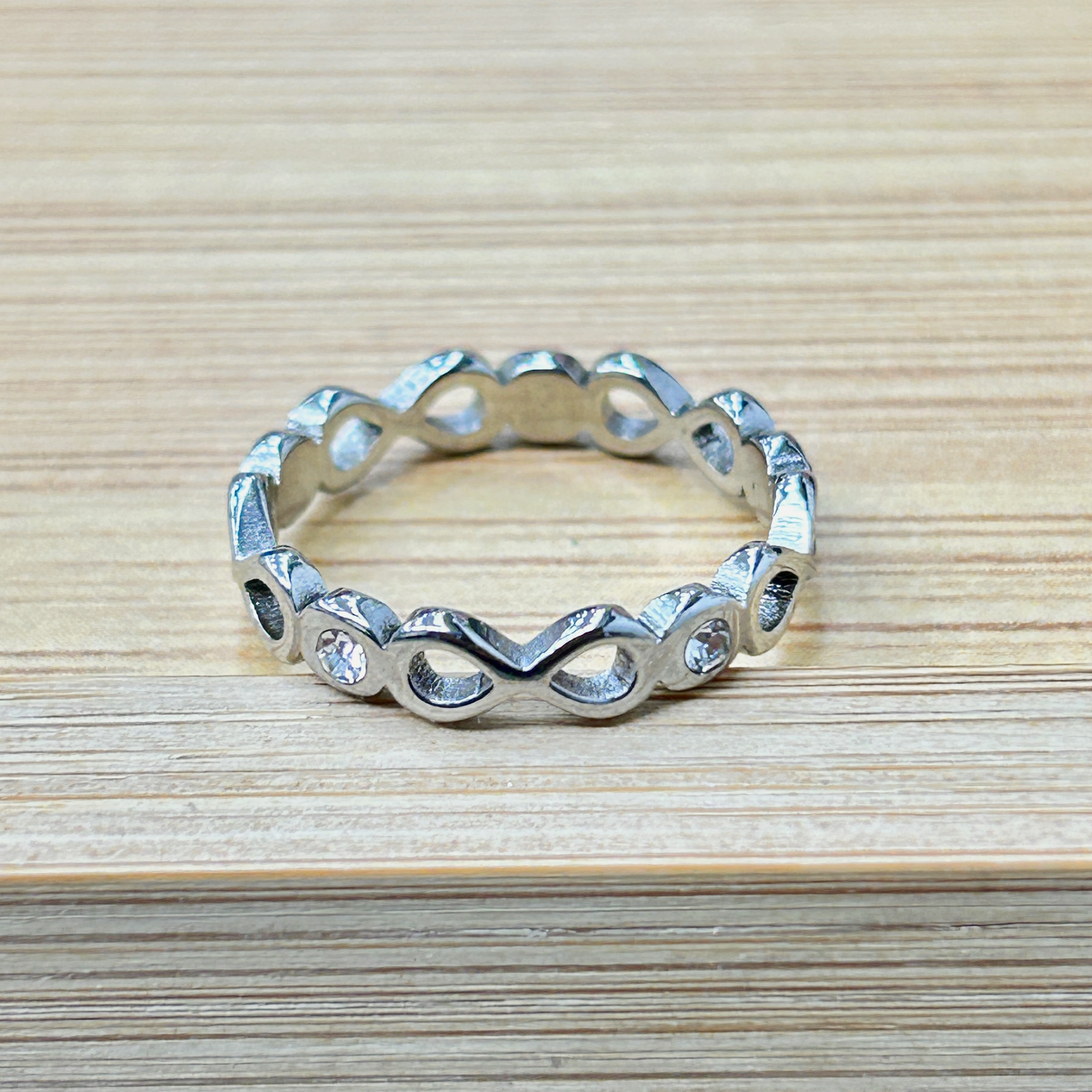 Silver Infinity Motif Zircon Eternity Ring picture2 - Eriy Gift Metallic chain bracelet with rounded links arranged in a circle on a light wooden surface, partially visible at the bottom of the photo.