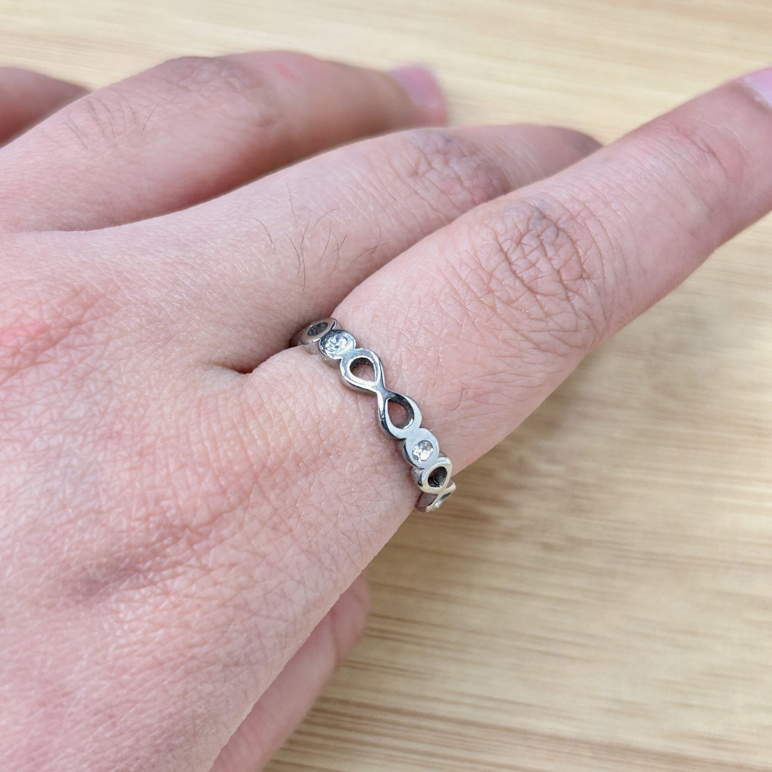 Silver Infinity Motif Zircon Eternity Ring - Eriy Gift Close-up of a wrist wearing a silver chain bracelet with evenly spaced circular links and small stones, resting on a wooden surface.
