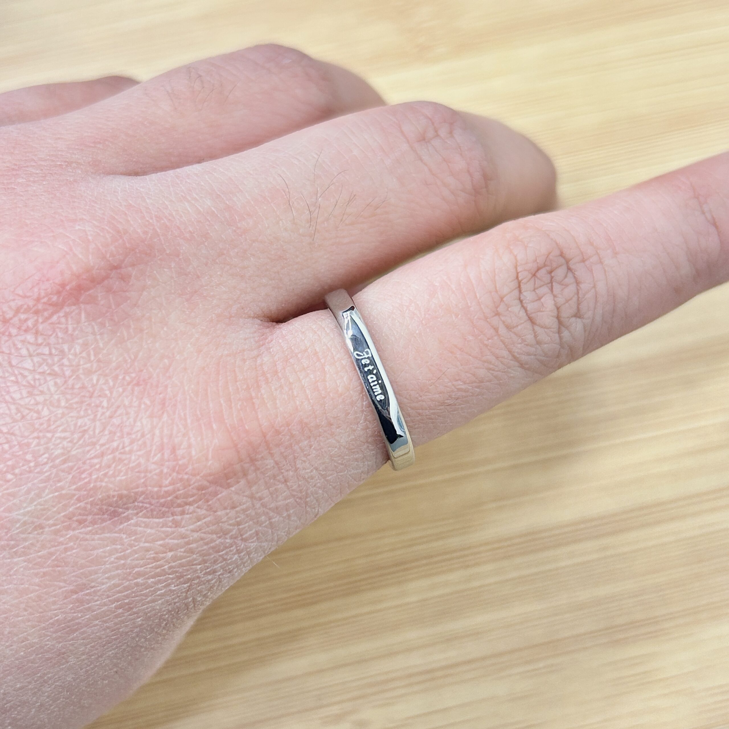 Close-up of a hand wearing a silver ring, resting on a light wooden surface.