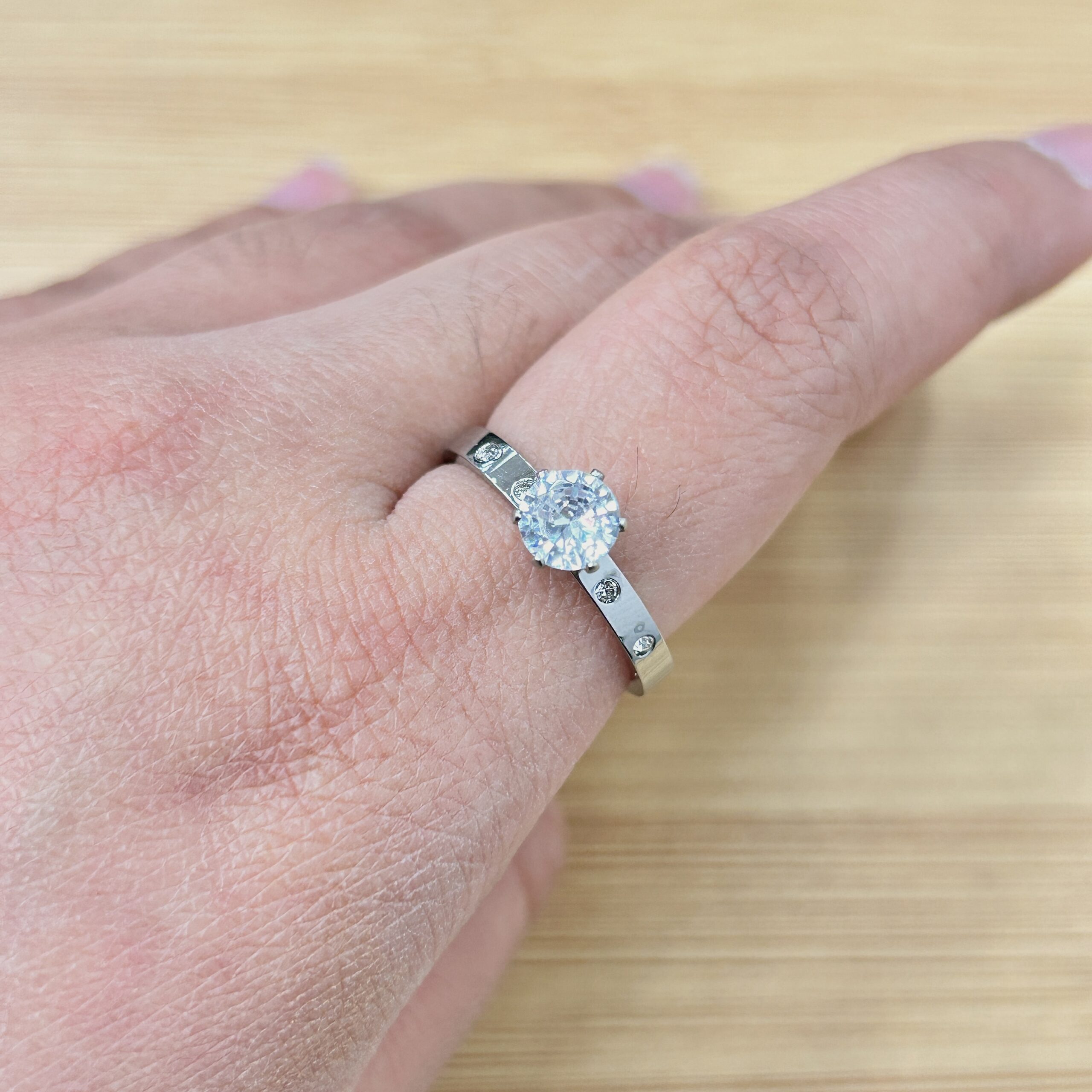 Close-up of a diamond engagement ring on the ring finger against a light wooden surface.