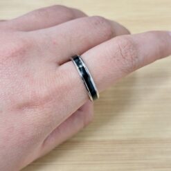 Close-up of a hand wearing a black-and-silver ring on the ring finger.