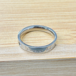 Close-up of a silver metal ring with 'Forever' engraved along the edge on a wooden surface.