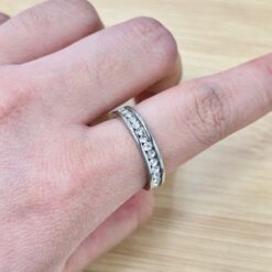 Close-up of a finger wearing a diamond-studded silver ring on a light wood surface.