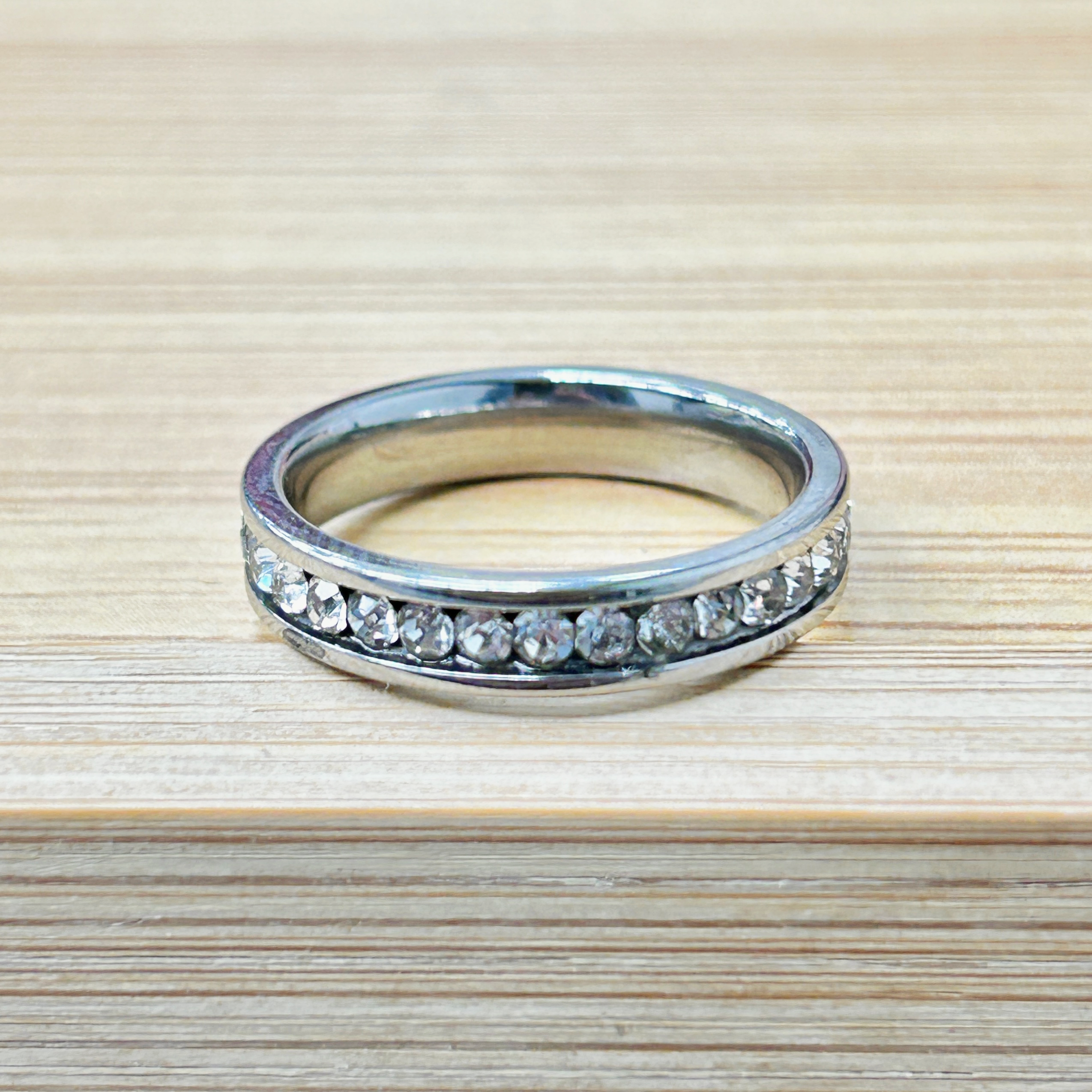 Single Row Round Zircon Channel Setting Ring picture2 - Eriy Gift Diamond-studded metal ring resting on a light wooden surface, photographed up close.