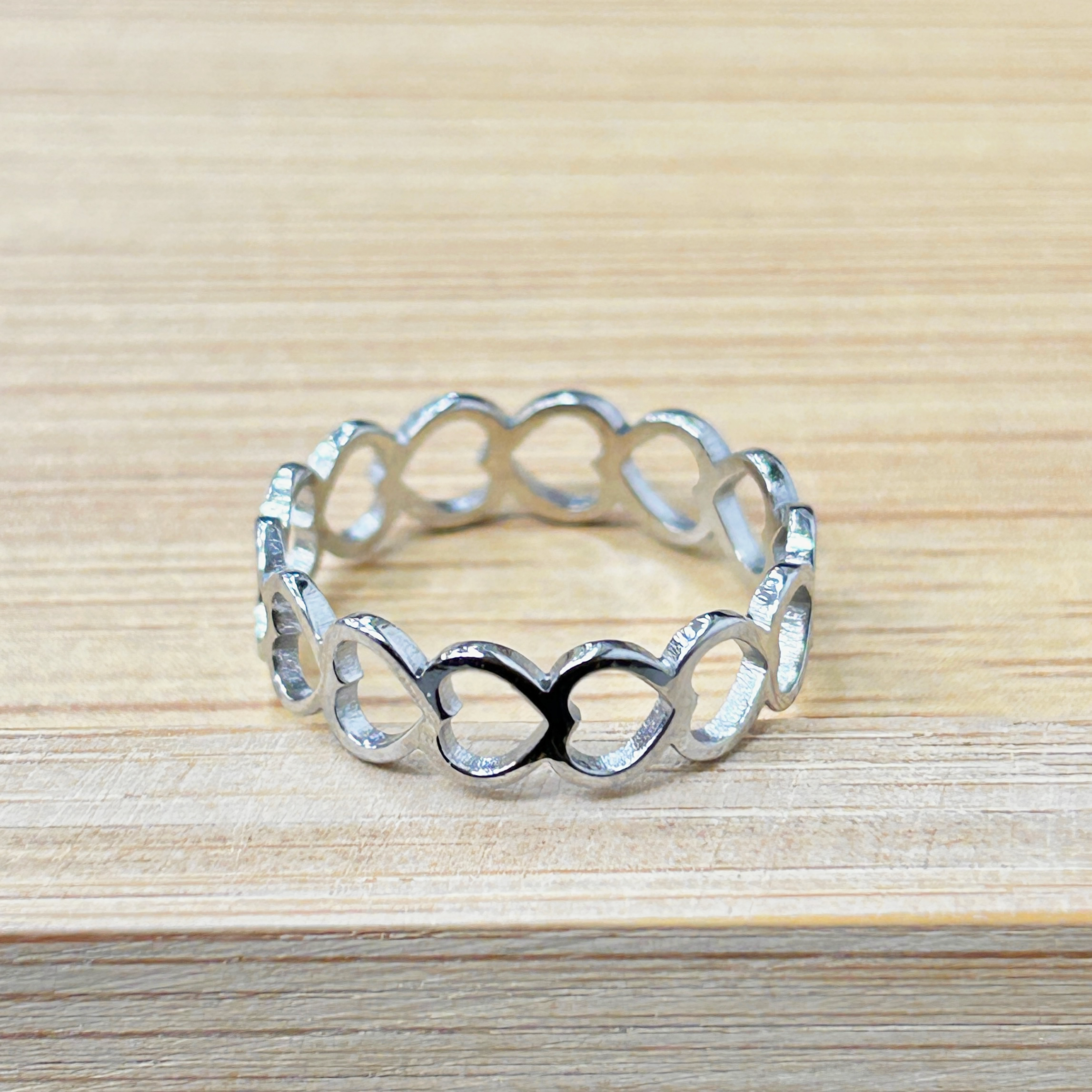 Sleek Silver Linked Hearts Cutout Ring picture2 - Eriy Gift Close-up of silver decorative metal loops arranged in a circular pattern on a pale wooden surface.