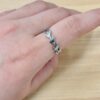 Close-up of a hand wearing a silver leaf-link bracelet on the wrist, with a light wooden background.