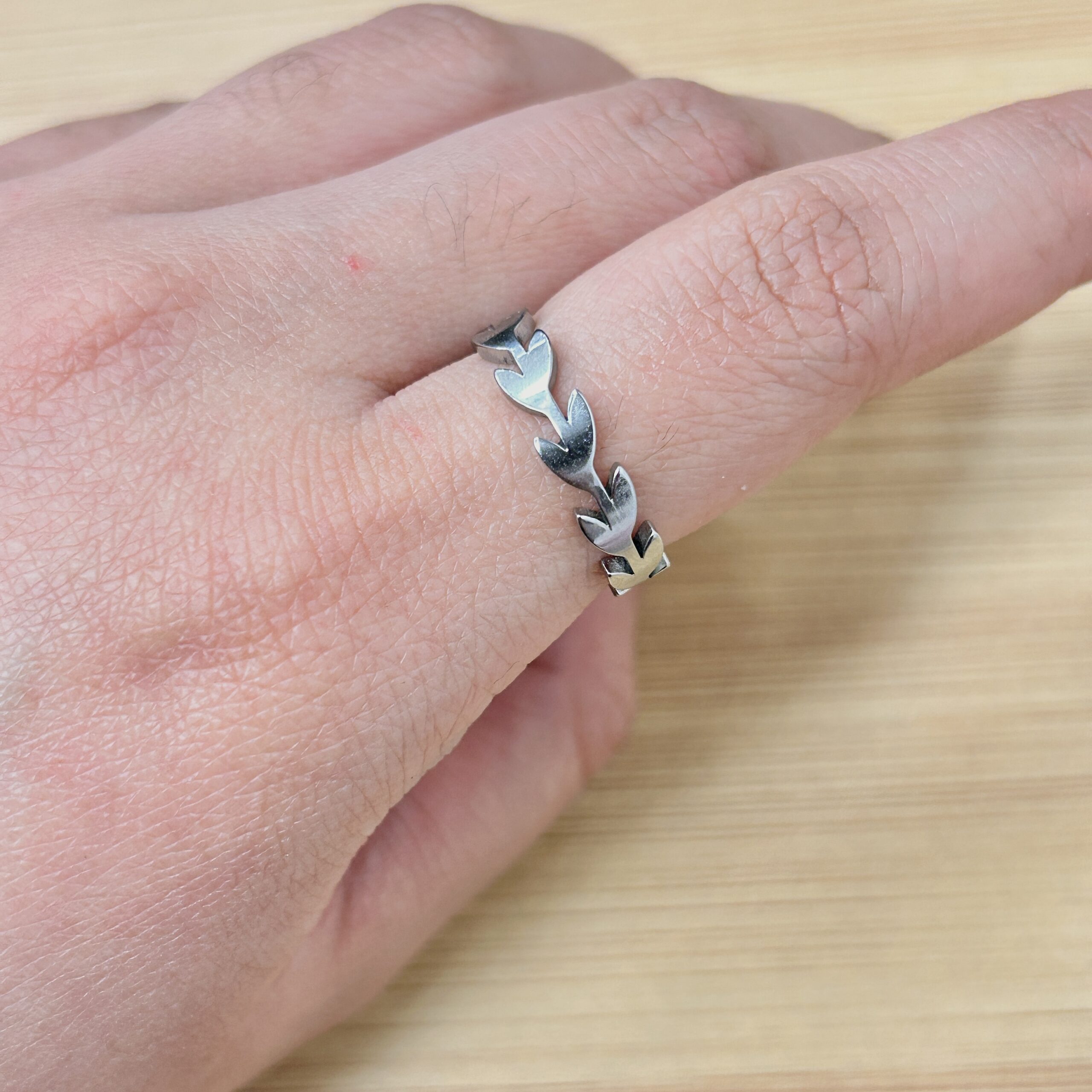Sleek Silver Olive Leaf Branch Ring - Eriy Gift Close-up of a hand wearing a silver leaf-link bracelet on the wrist, with a light wooden background.