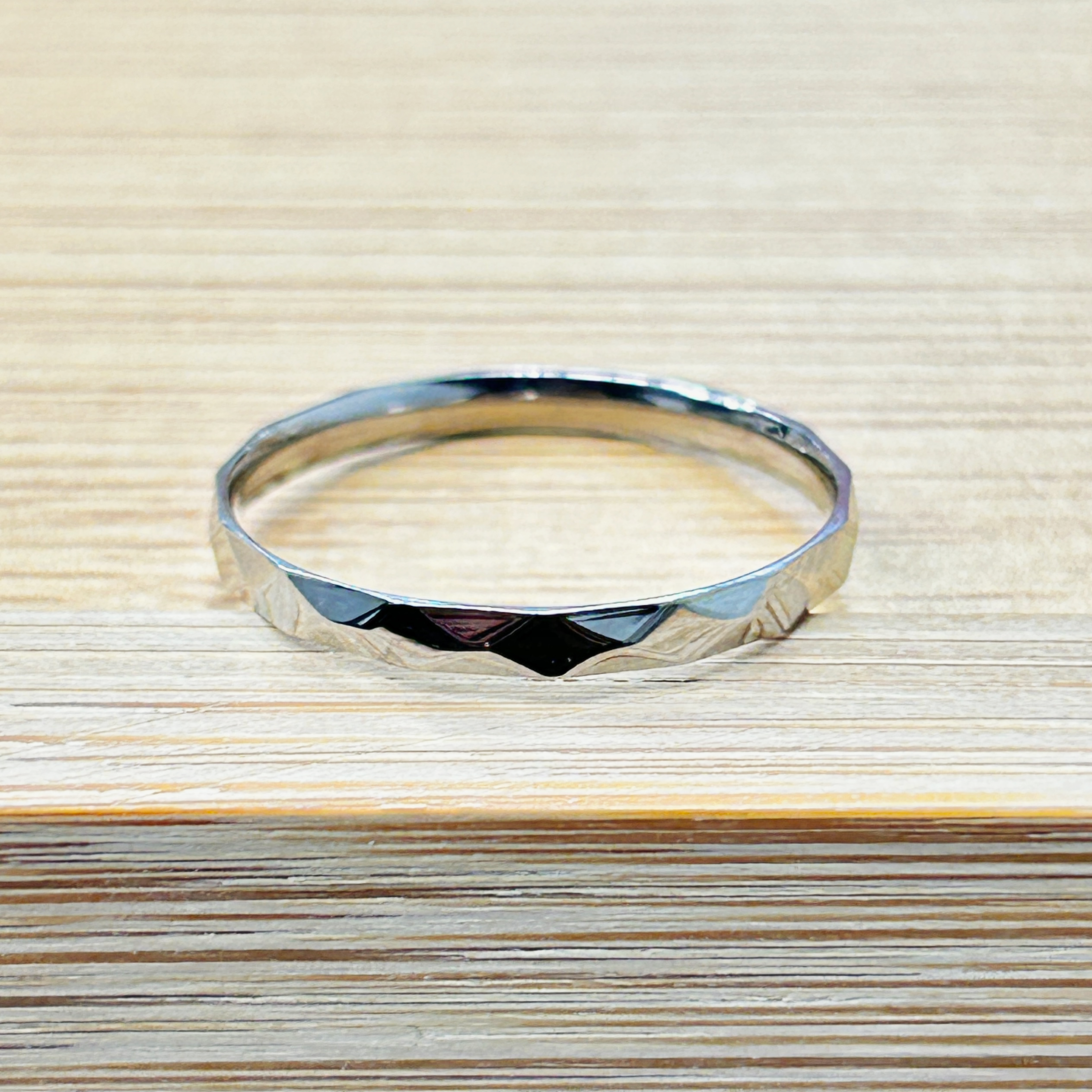 Sleek Silver Thin Faceted Stackable Ring picture2 - Eriy Gift Silver metal bracelet resting on a light wooden surface, viewed from above.