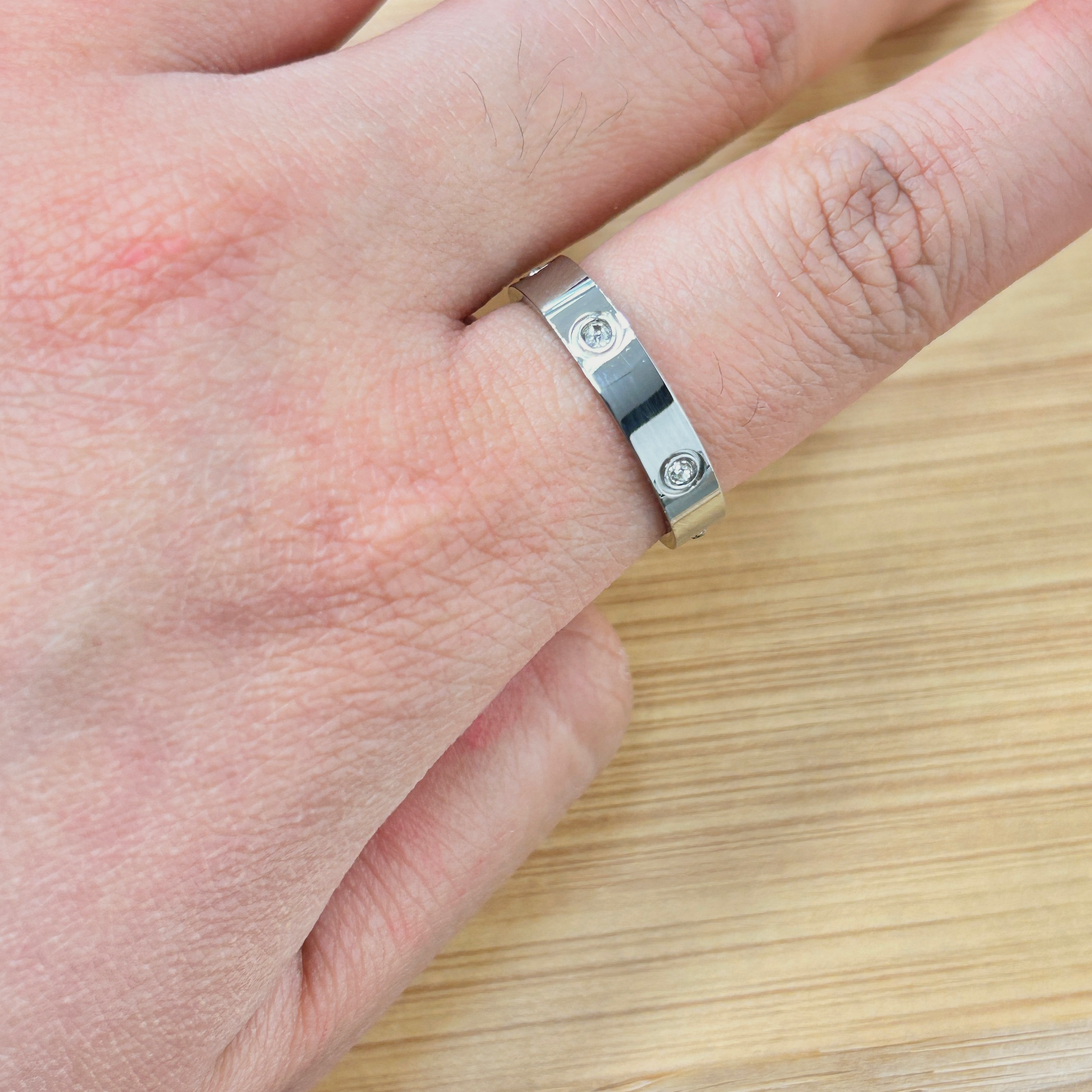 Close-up of a hand wearing a silver metal ring with visible screws on the finger, wooden surface in the background.