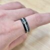 Close-up of a finger wearing a black metal ring with a row of clear diamonds set into the band.