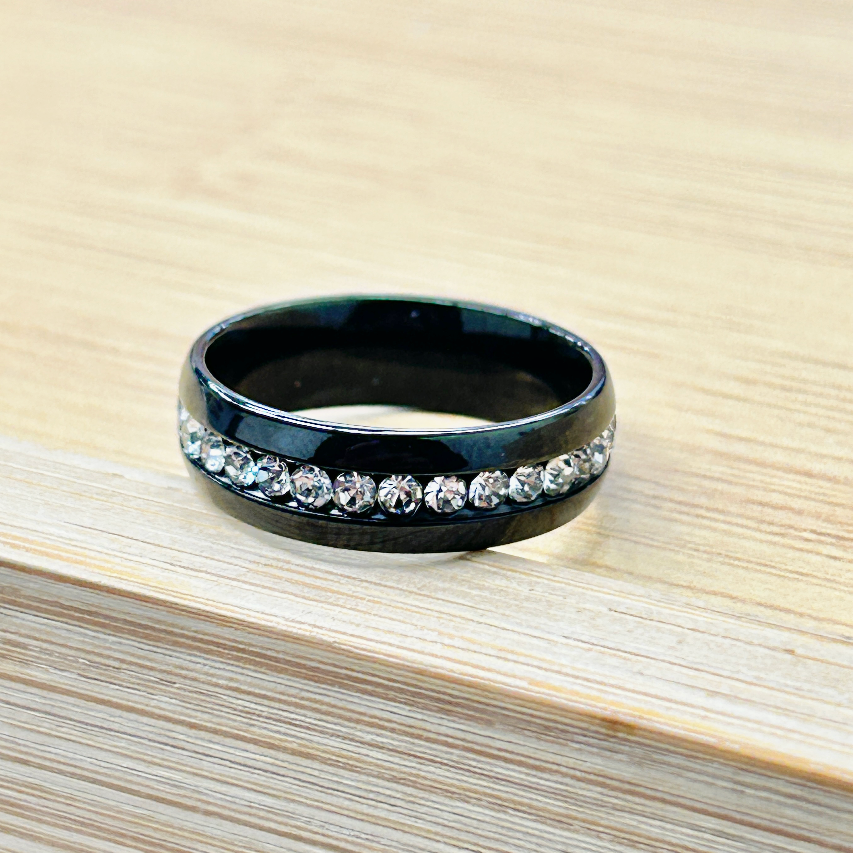 Diamond-studded ring with a dark band resting on a light wooden surface.