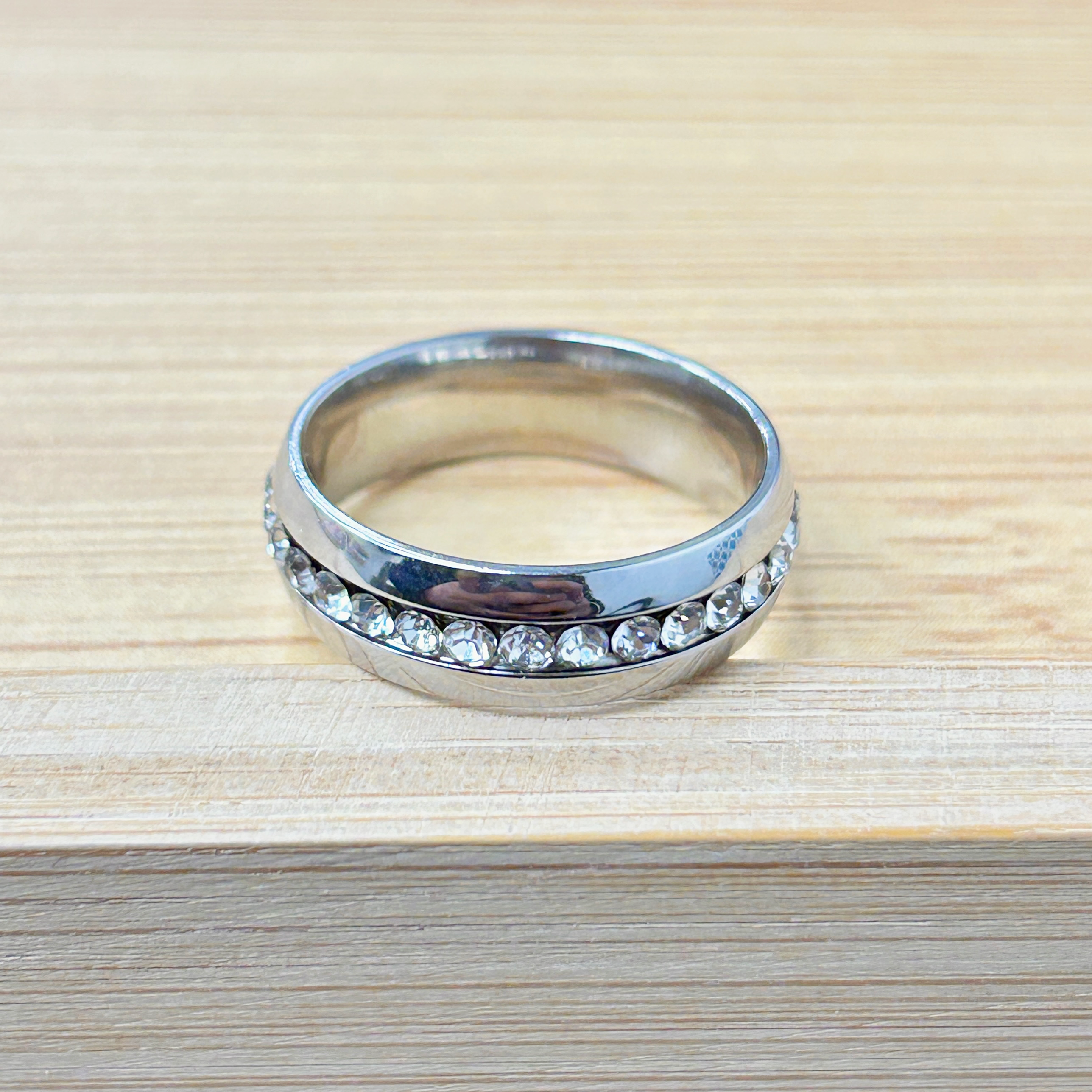 Close-up of a silver ring with faceted stones set around the band on a light wood surface.