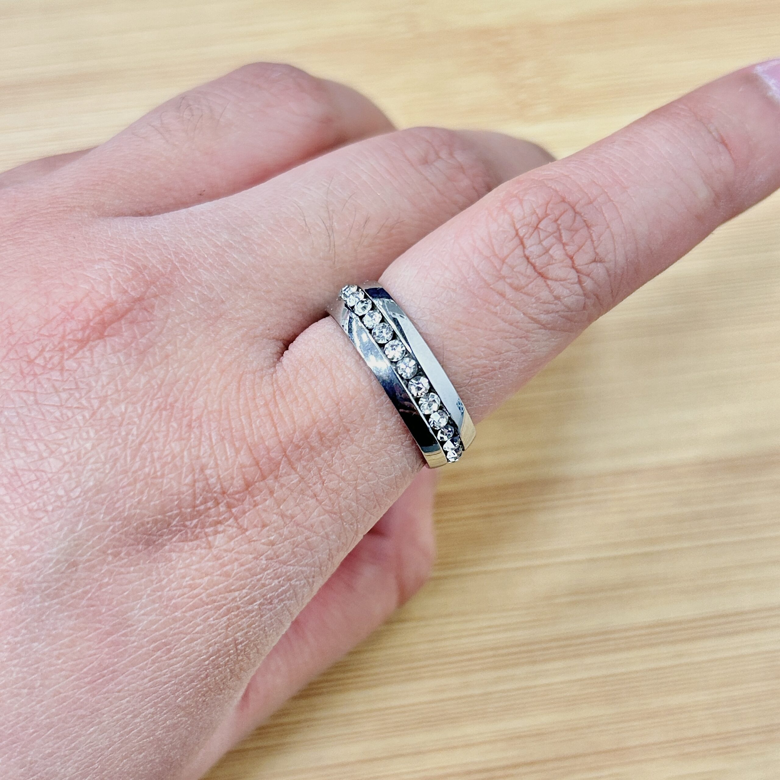 Close-up of a silver diamond ring worn on the ring finger, with a light wooden surface in the background.