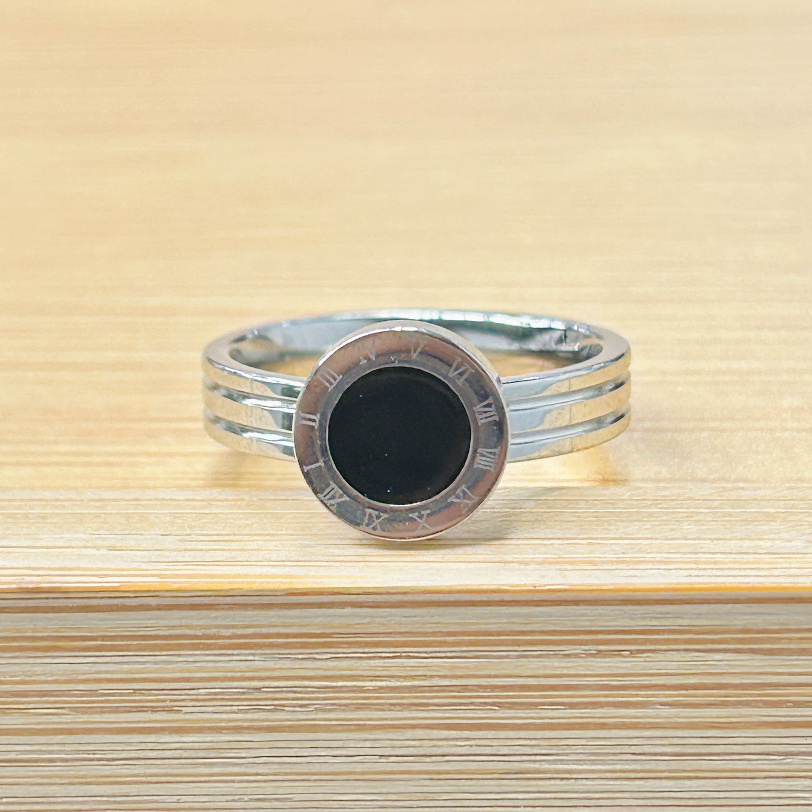 Close-up of a silver ring with a black center and Roman numeral engravings around the rim on a wooden surface.