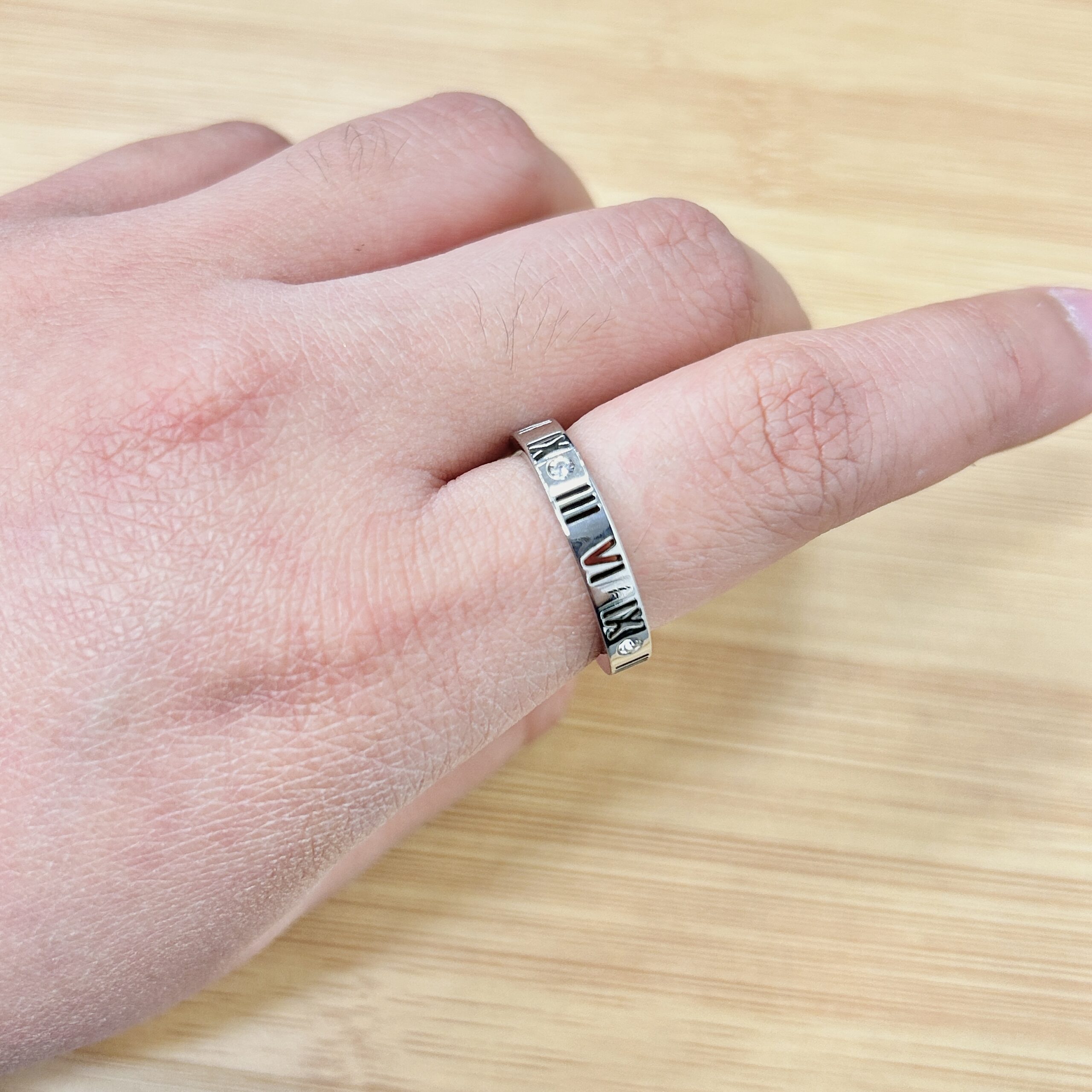 Thick Silver Roman Numeral Zircon Ring - Eriy Gift Close-up of a silver engraved ring on a finger, with a light wooden surface in the background.
