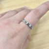 Close-up of a hand wearing a silver textured ring with a small gemstone on the ring finger, on a wooden surface.