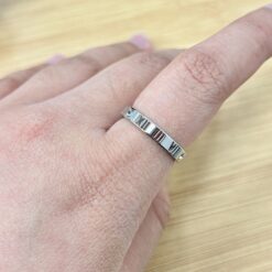 Thin Silver Cutout Roman Numeral Zircon Ring - Eriy Gift Close-up of a hand wearing a silver textured ring with a small gemstone on the ring finger, on a wooden surface.