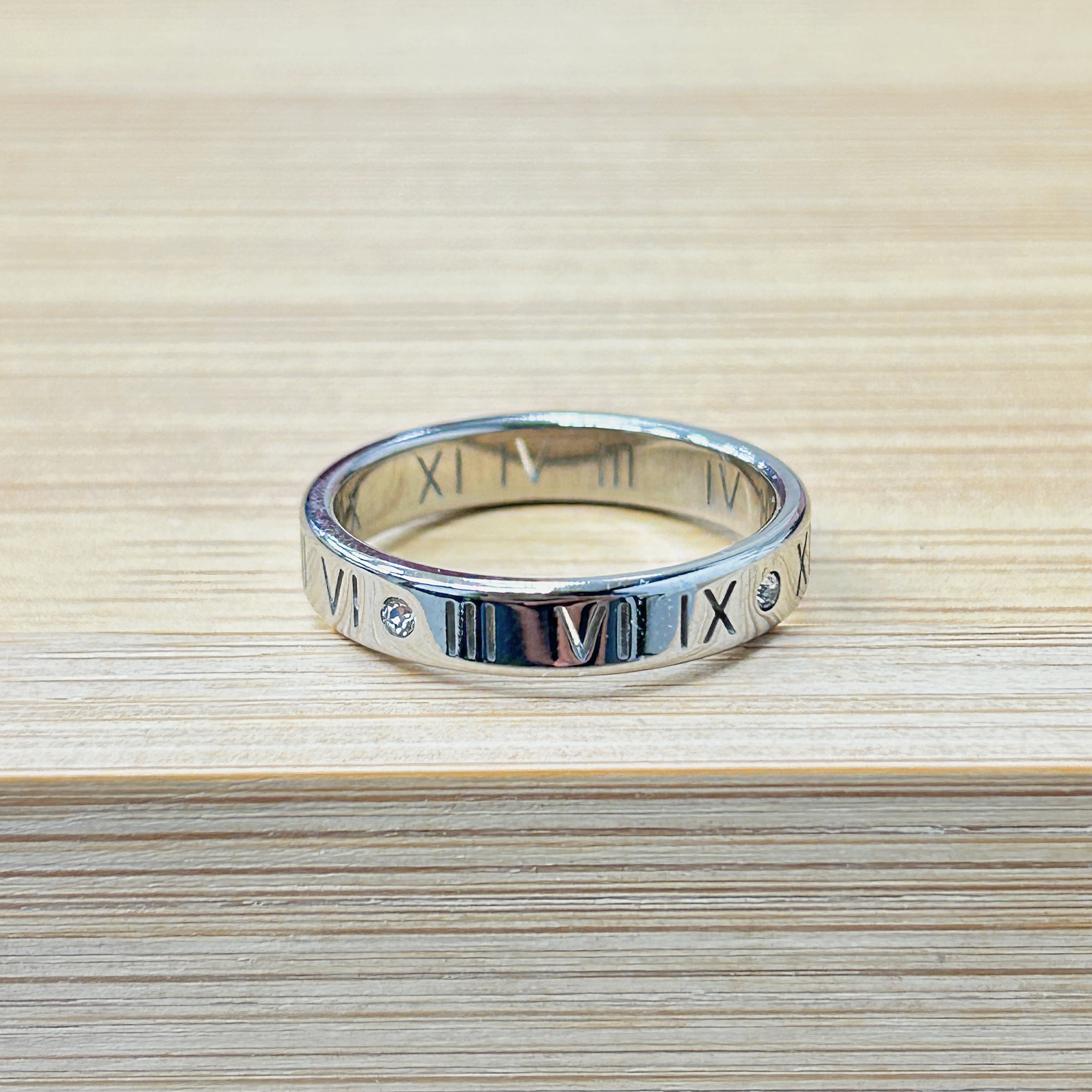 Thin Silver Roman Numeral Zircon Ring picture2 - Eriy Gift Close-up of a silver ring with Roman numerals engraved around its band on a light wooden surface.