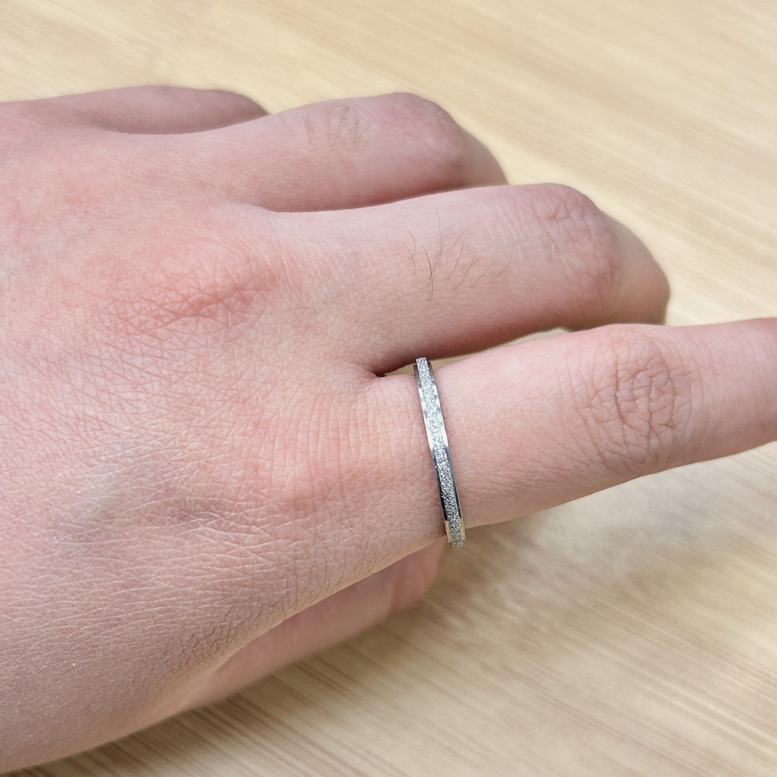 Thin Silver Sandblast Glitter Promise Ring - Eriy Gift Close-up of a wrist wearing a textured silver bracelet over bare skin, wood tabletop in the background.