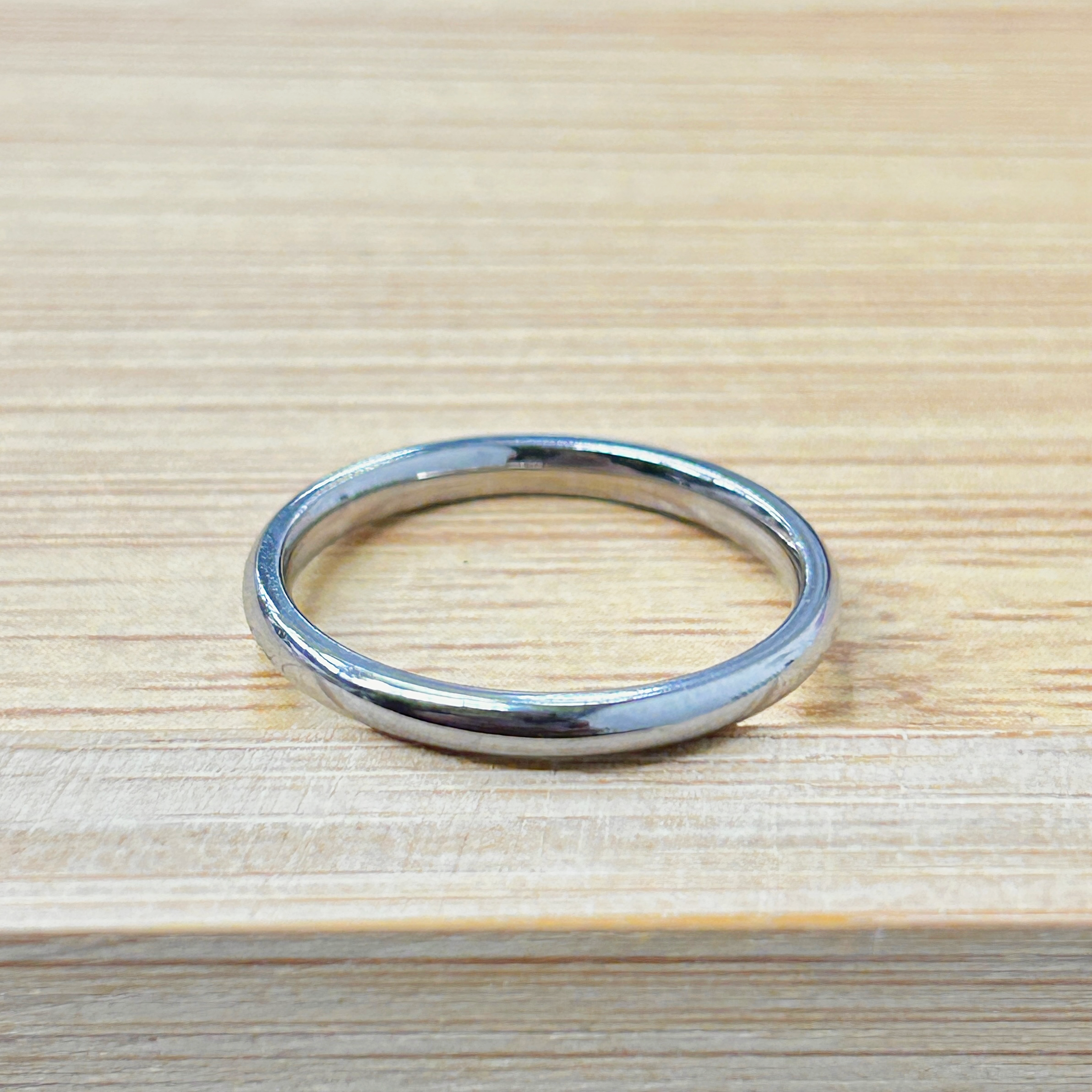 Timeless Polished Silver Thin Promise Ring picture2 - Eriy Gift Close-up of a silver metal ring on a light wooden table surface.