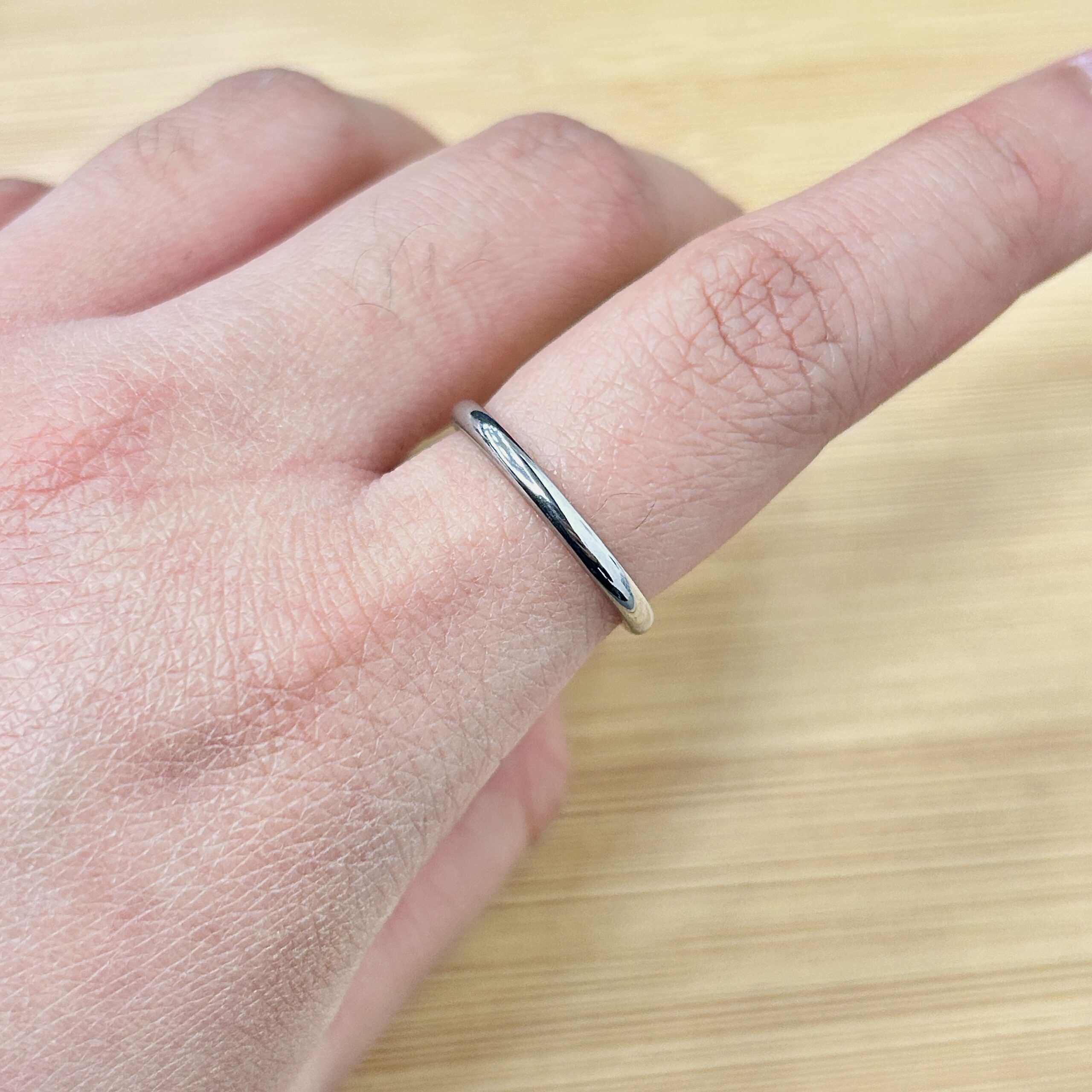 Timeless Polished Silver Thin Promise Ring - Eriy Gift Close-up of a hand wearing a slim silver ring with a small dark gemstone on the ring finger, against a light wooden background.