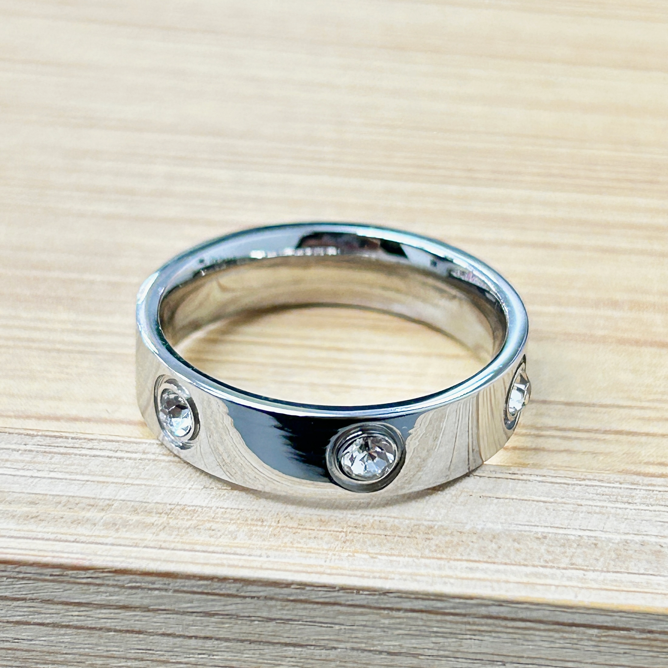 Wide Band Silver Zircon Set Ring picture2 - Eriy Gift Close-up of a chrome-plated pipe clamp with screws on a light wood surface (tabletop).
