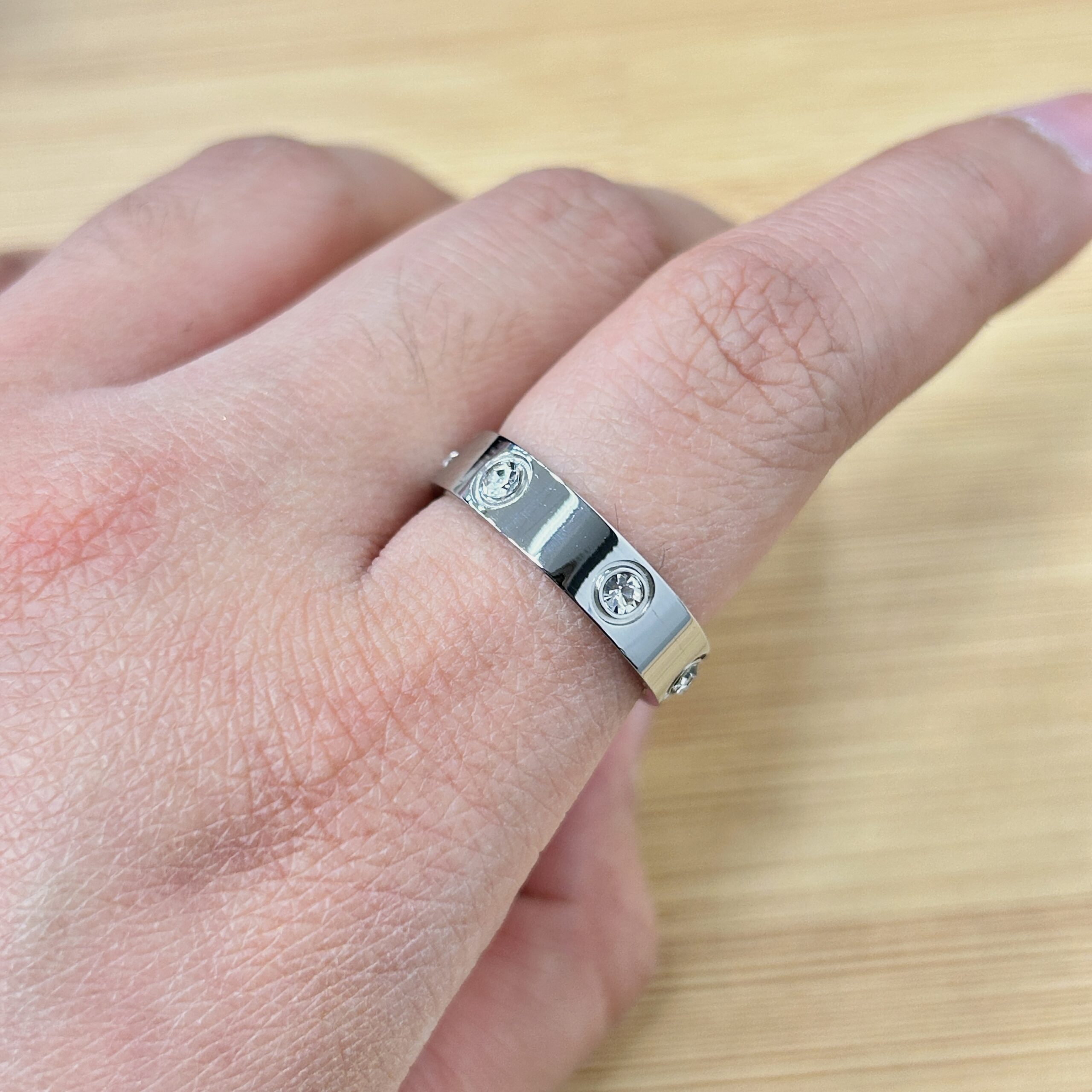 Wide Band Silver Zircon Set Ring - Eriy Gift Close-up of a hand wearing a silver ring with a screw-head motif on a light wooden surface.