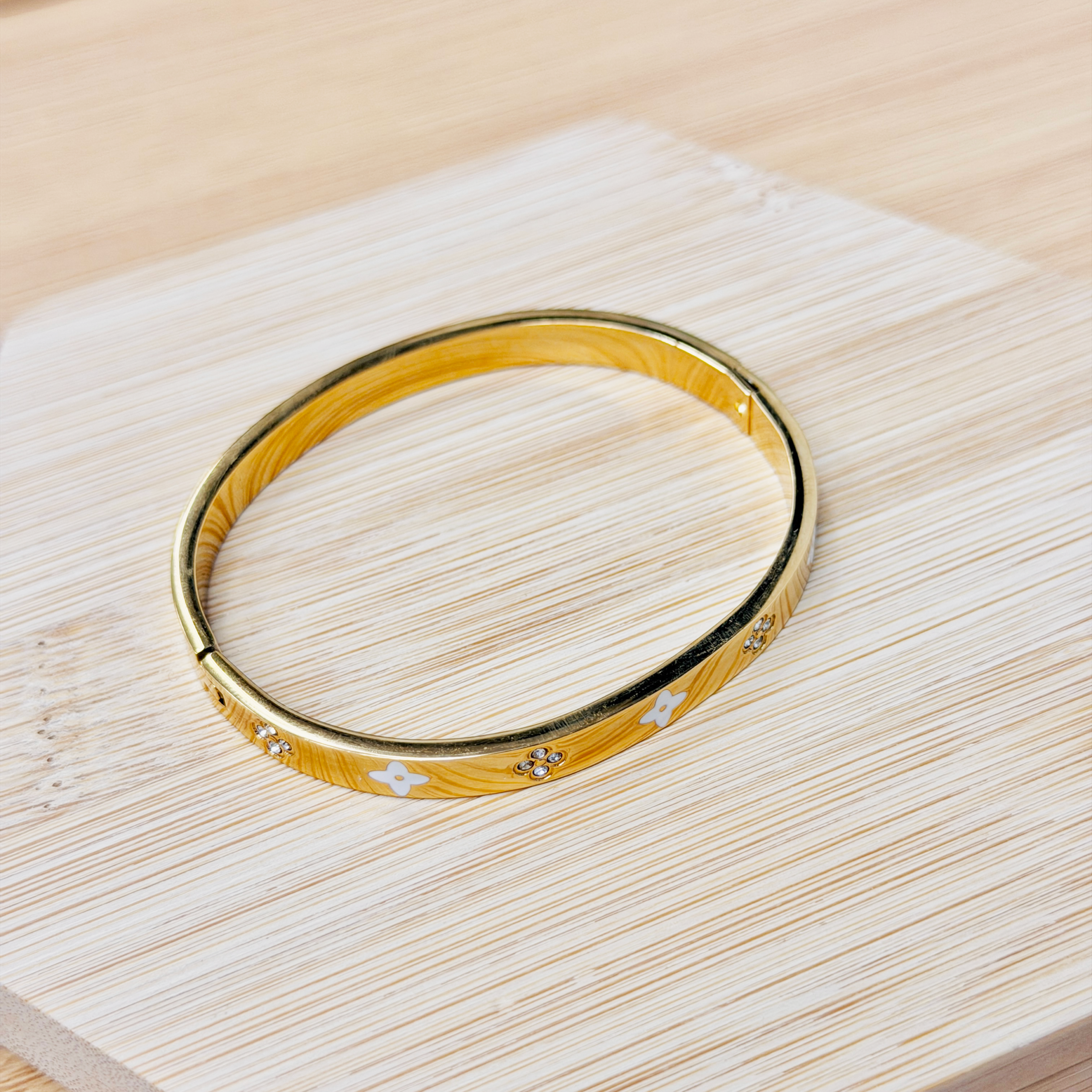 Gold-toned bangle bracelet with white flower motifs on a light wood surface
