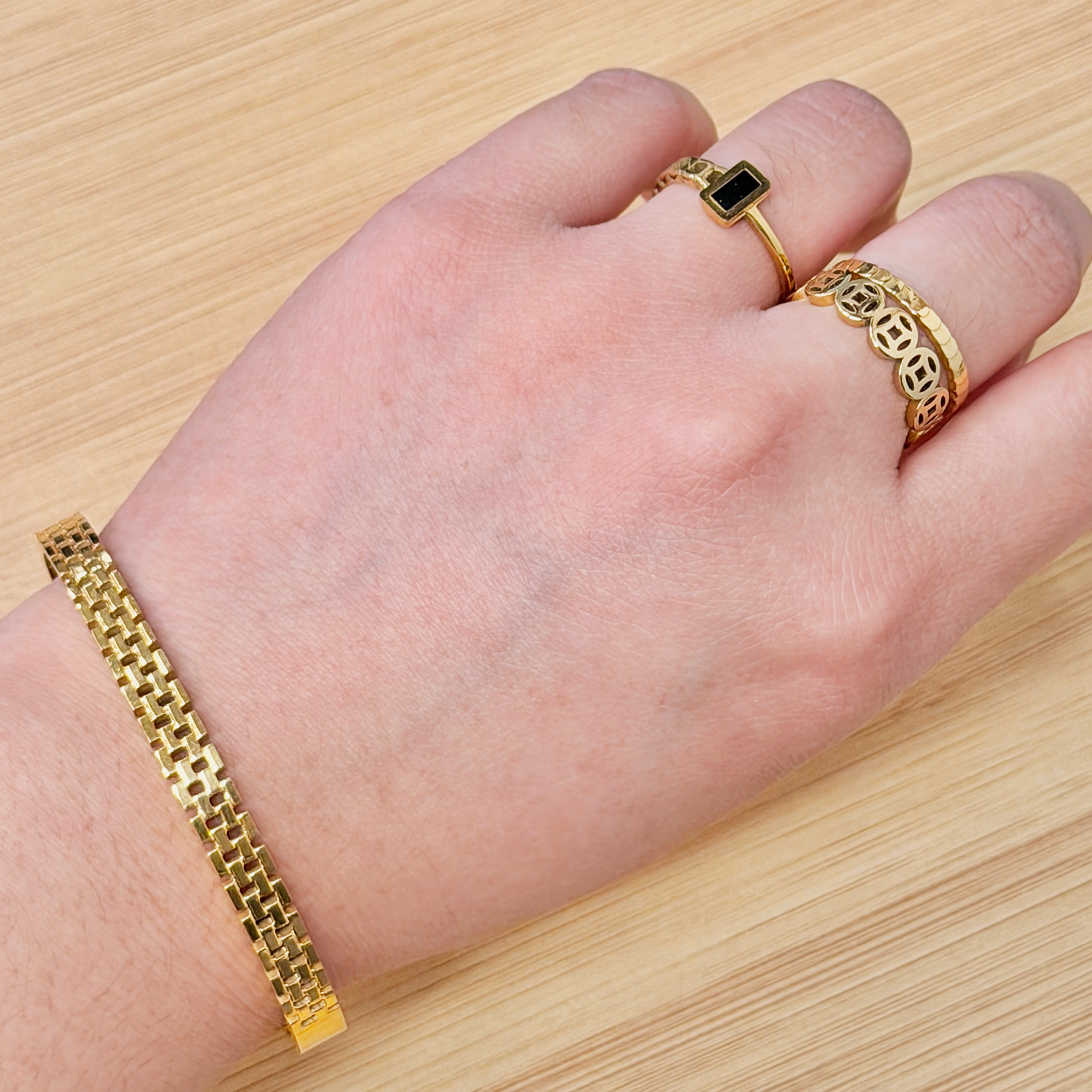Close-up of a hand wearing a gold bracelet and a ring with a black rectangular stone on the finger and wrist.
