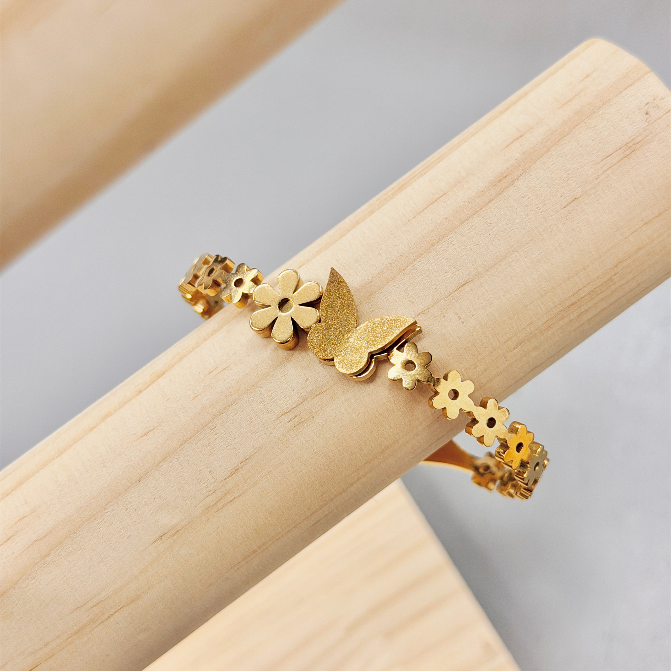 Elegant Gold Floral Band Butterfly Bangle picture3 - Eriy Gift Close-up of gold floral and star-shaped jewelry links laid along a light wooden surface edge.