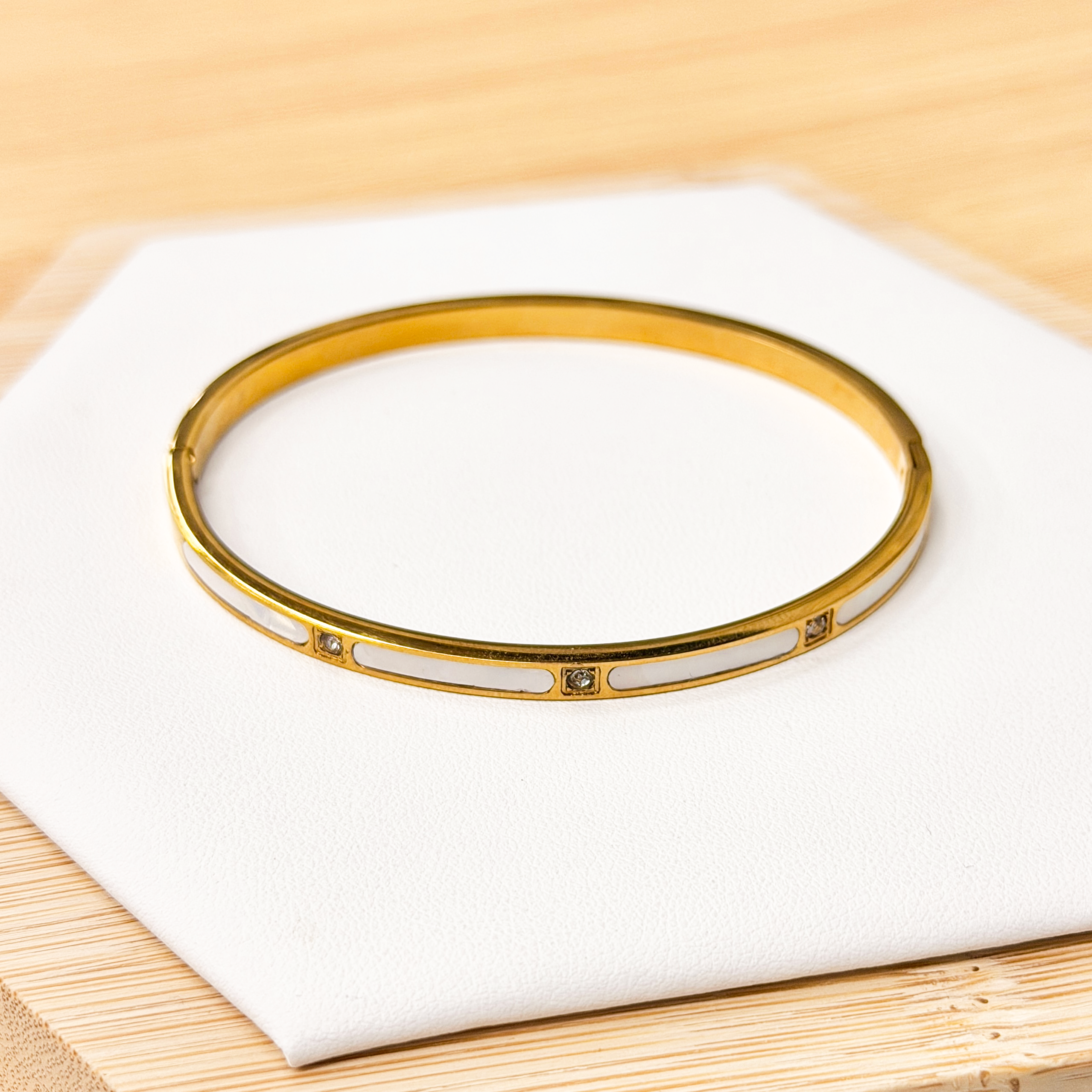 Elegant Gold Tone Opalescent Stone Inlay Bangle picture1 - Eriy Gift Gold bracelet with small diamonds on a white display surface over a light wood background
