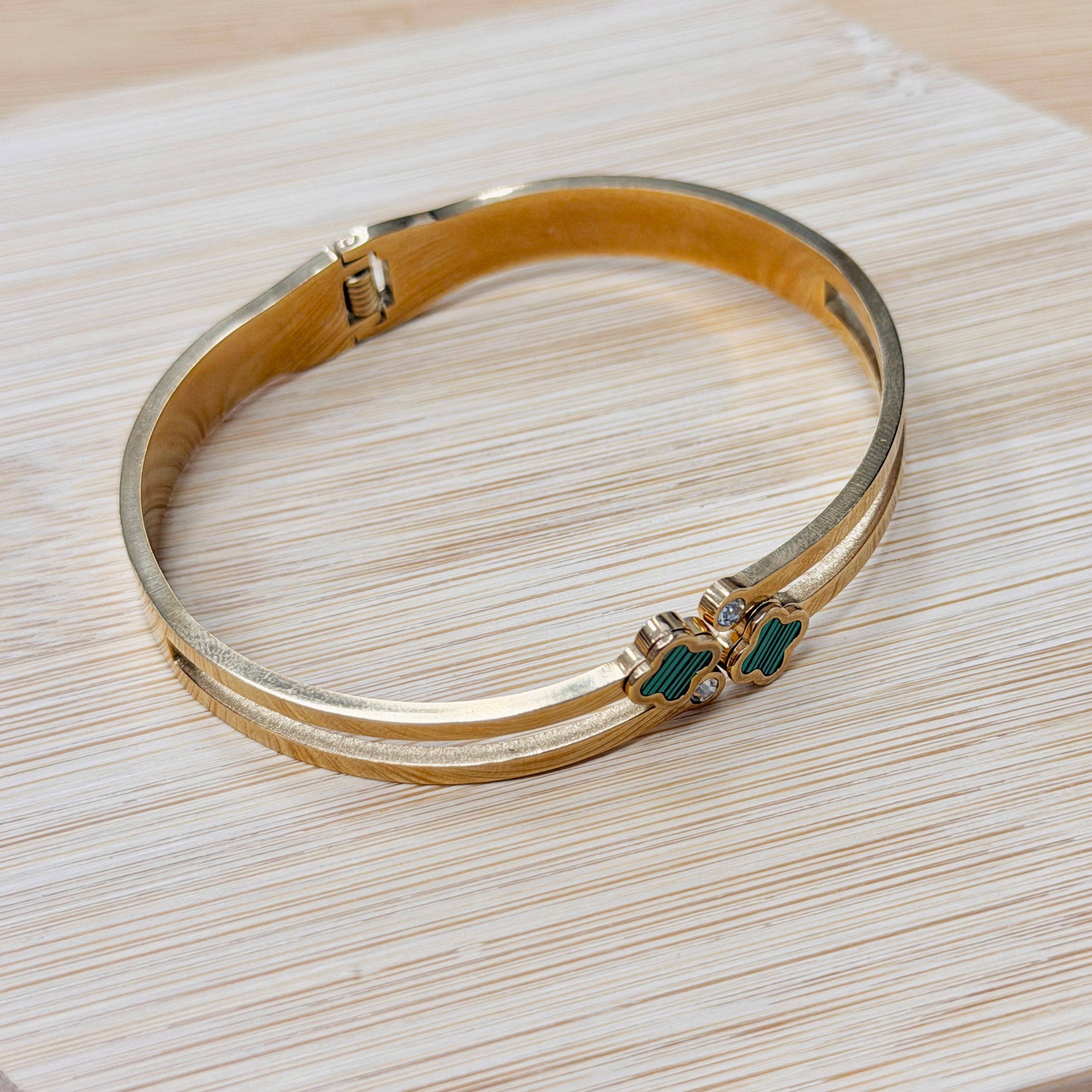 Close-up of a gold-toned bracelet with turquoise enamel clover inlays resting on a light wood surface, curved along the grain.