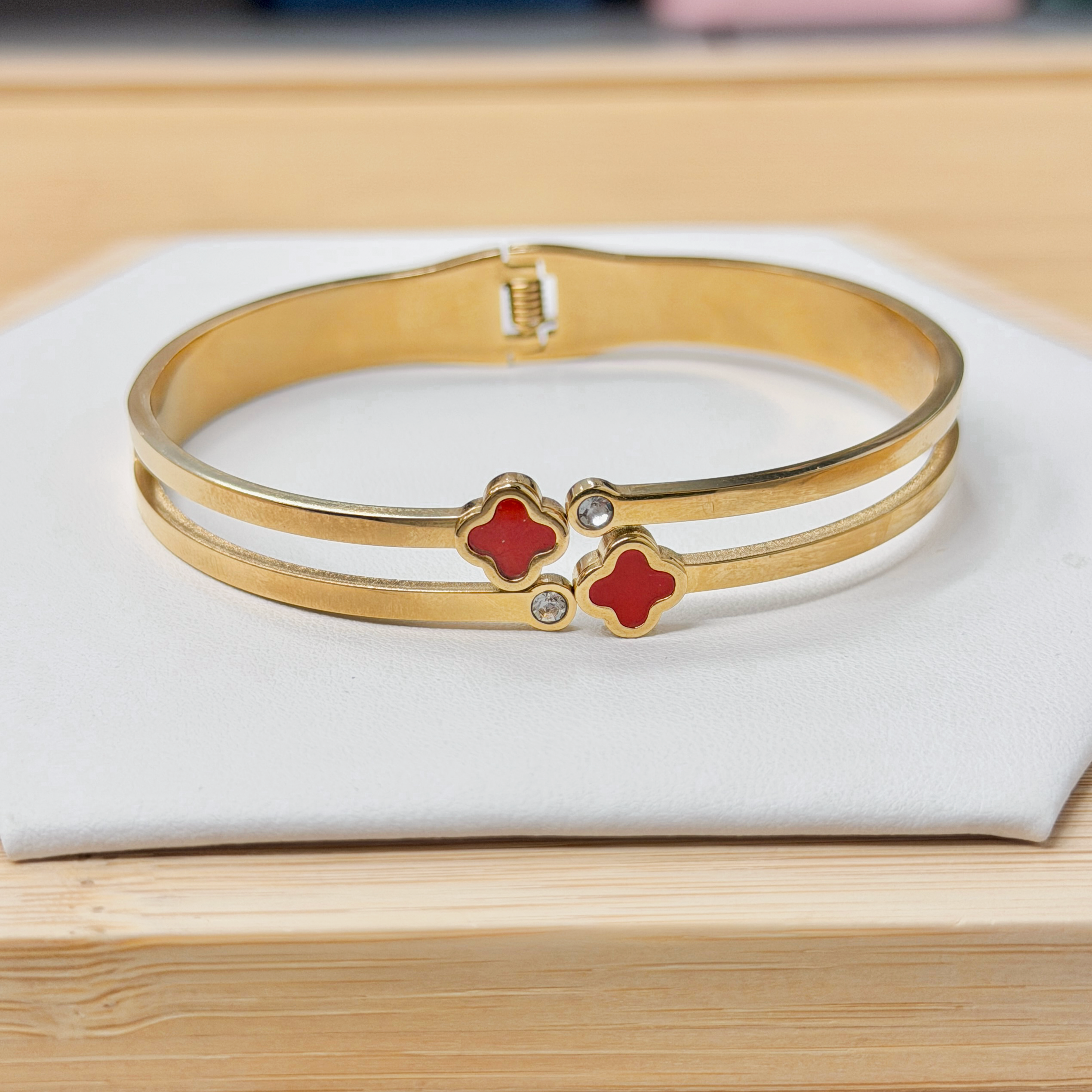Gold Double Band Dual Red Clover Bangle picture2 - Eriy Gift Close-up of gold bangles with red clover-shaped charms resting on white fabric.