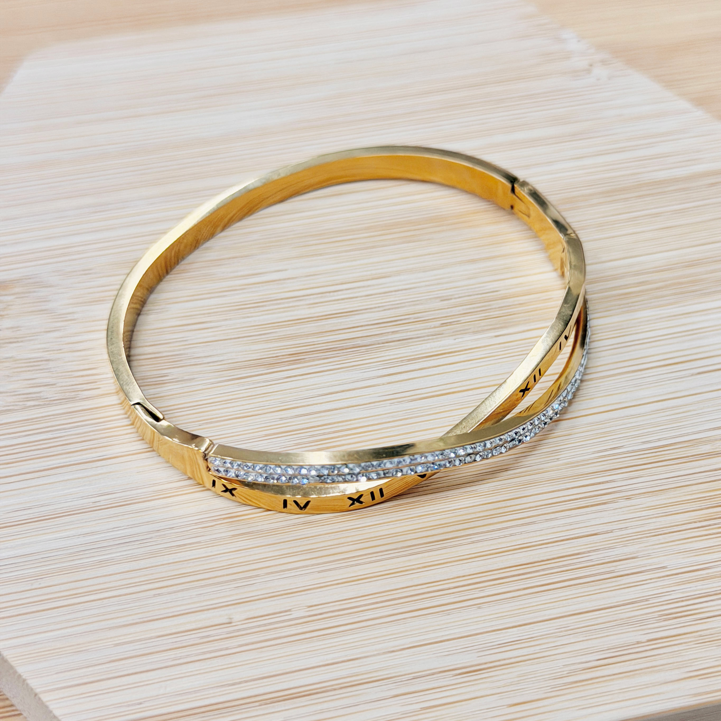 Gold bracelet with small diamonds resting on a light wooden surface nearby the edge of the frame.
