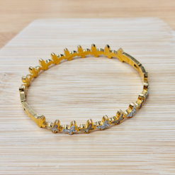 Gold-toned gear-shaped bracelet with a rhinestone segment on a light wood surface.