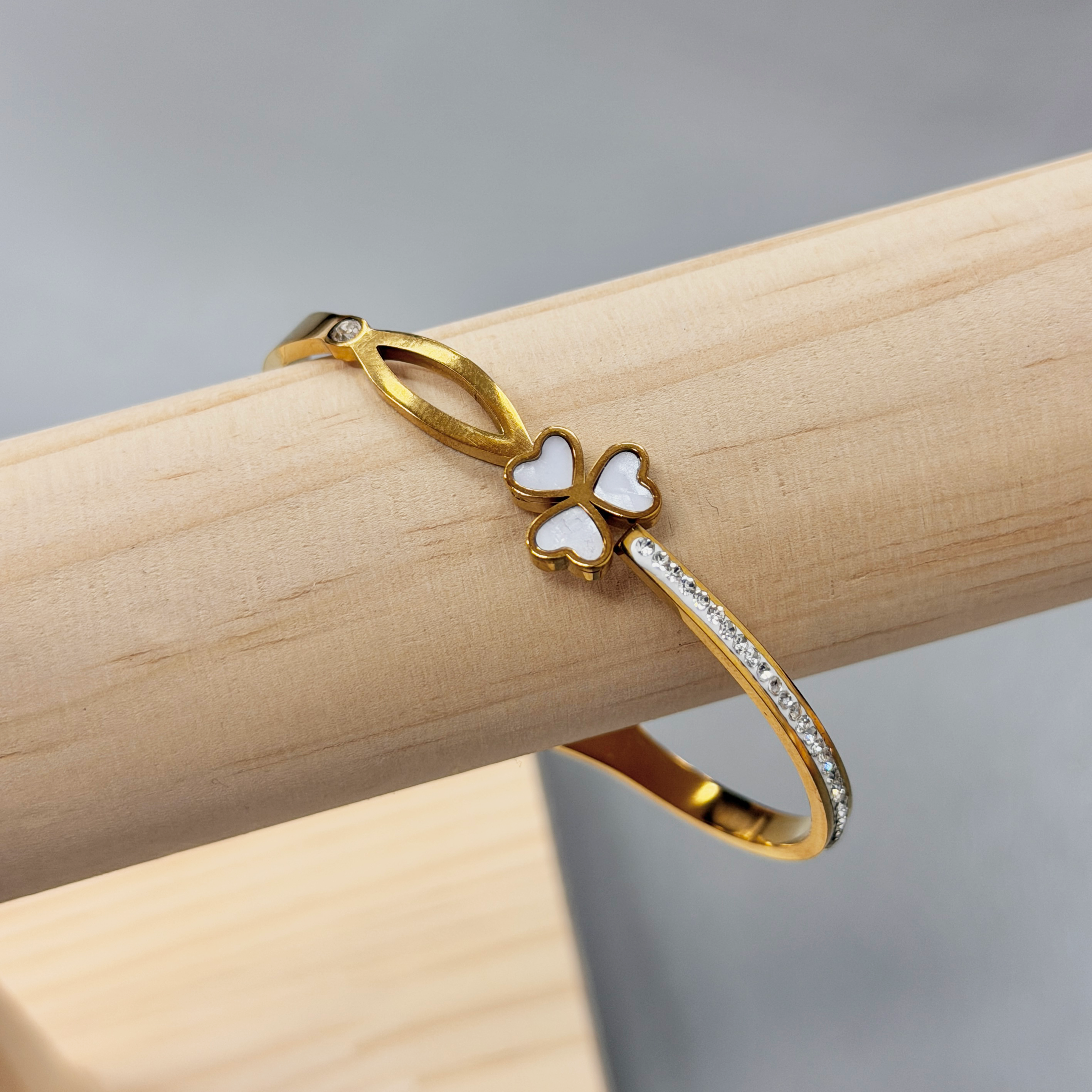 Gold ring with butterfly-shaped charms resting on a light wooden block, against a soft gray background.