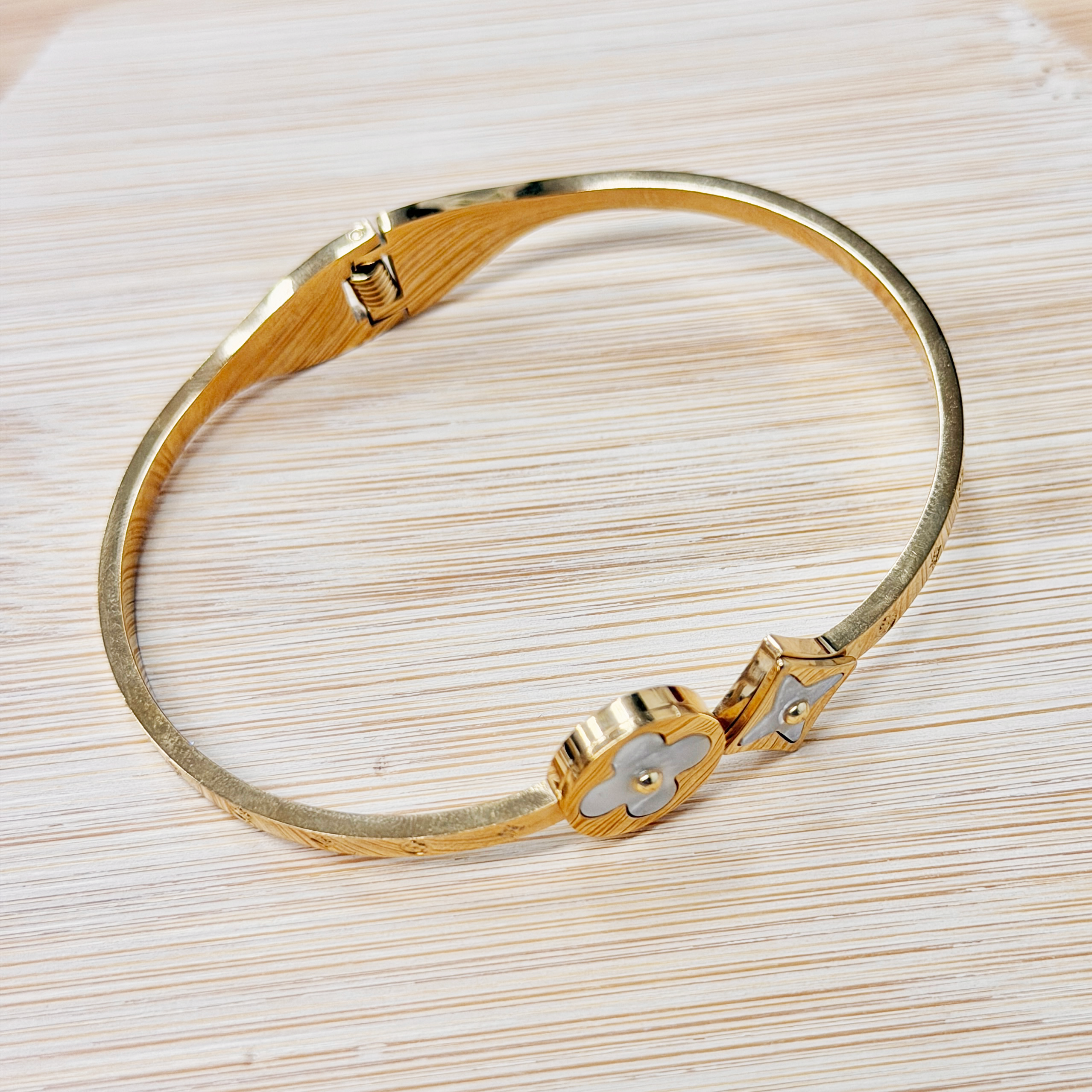 Gold metal bracelet with a hinge clasp resting on a light wooden surface.
